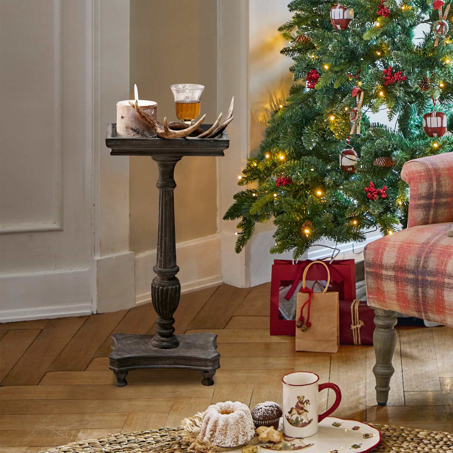 Table d'appoint Caren Piedestal en bois foncé avec bougie et décor en bois de cerf près d'un sapin de Noël décoré et cadeaux