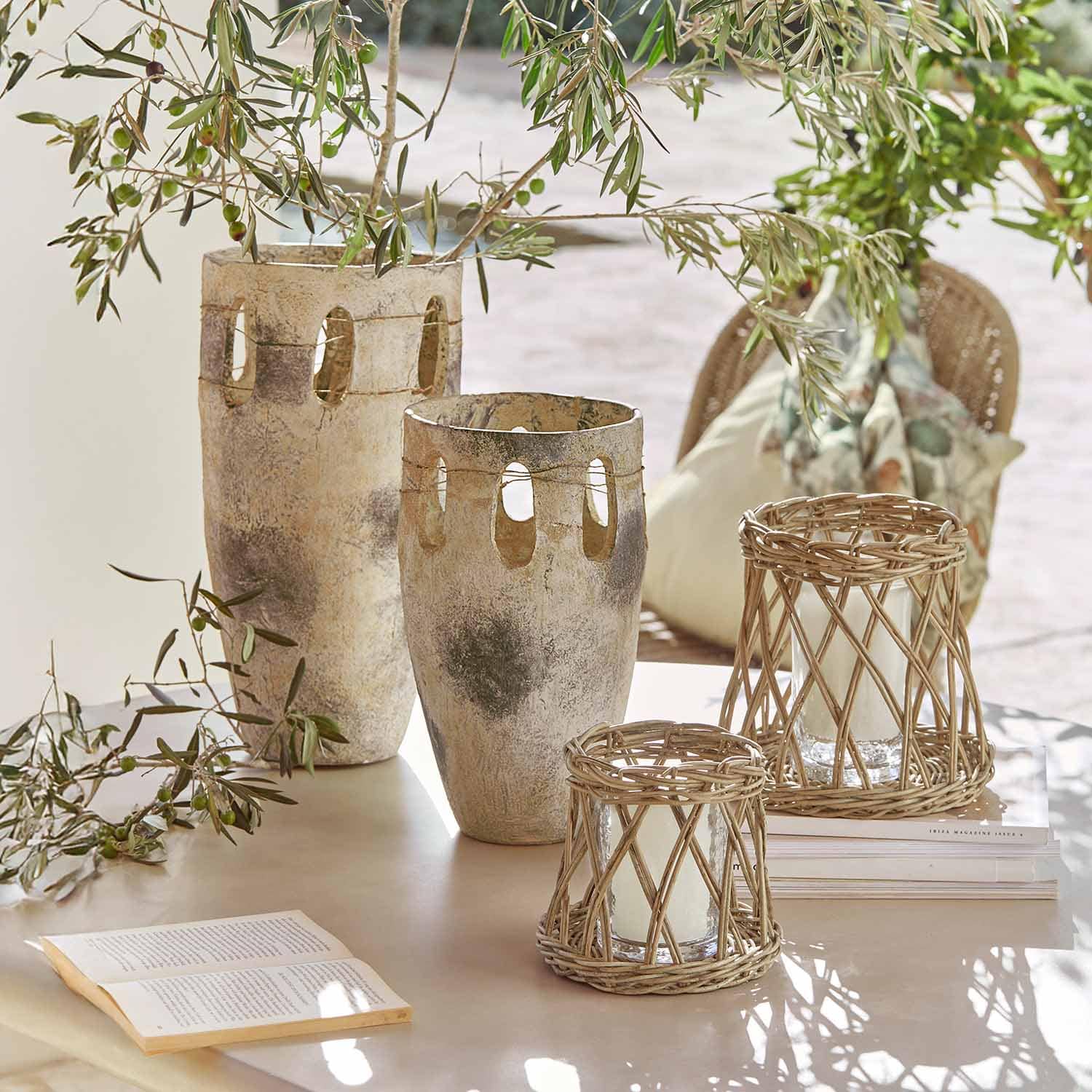 Deux grands vases en céramique et deux lanternes en rotin sur une table avec des branches vertes et un livre ouvert