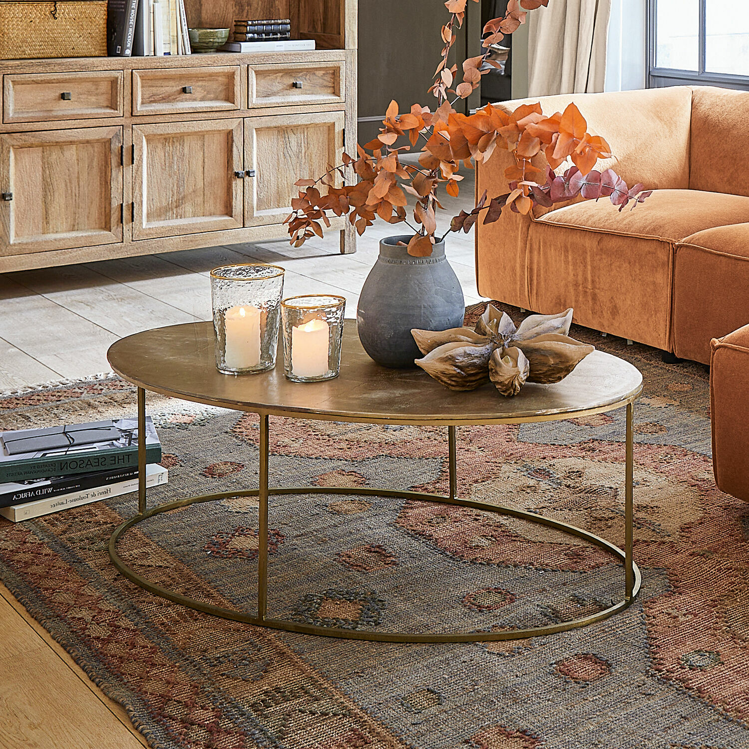 Table basse Leron Table basse ovale avec plateau en métal couleur laiton sur tapis dans un salon avec canapé orange