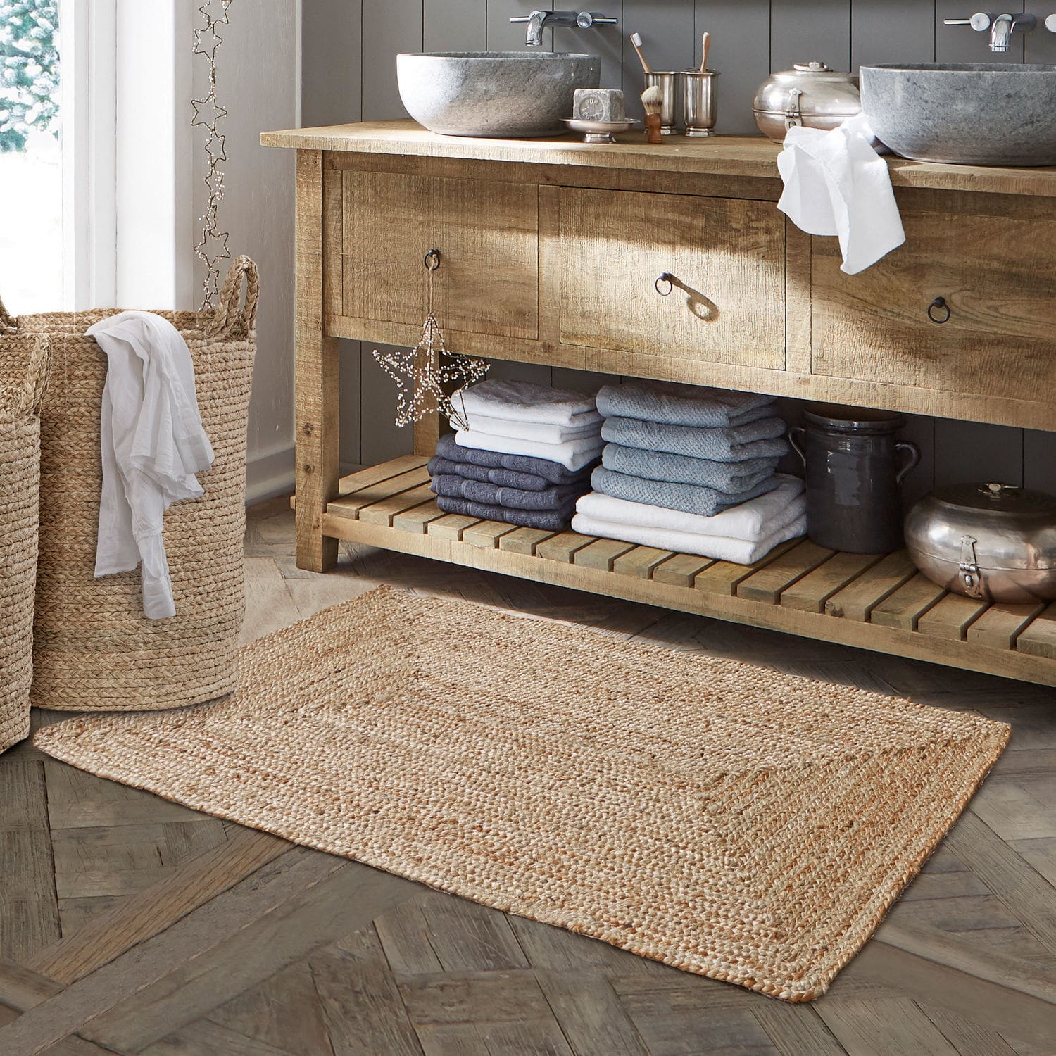 Tapis de bain Busselton Tapis de salle de bain en jute naturelle beige posé sur un sol en bois avec panier à linge tressé