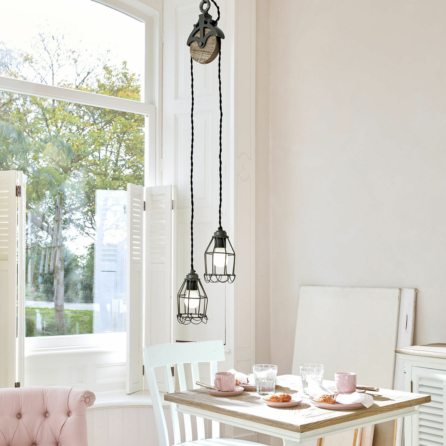 Suspension Trevici Deux suspensions en métal noir avec cage protectrice au-dessus d'une table en bois dans un intérieur lumineux