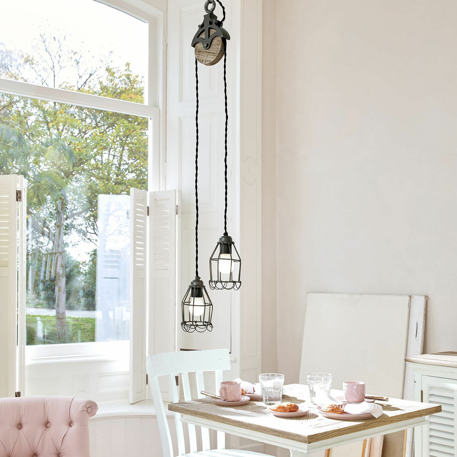 Suspension Trevici Deux suspensions en métal noir avec cage protectrice au-dessus d'une table en bois dans un intérieur lumineux