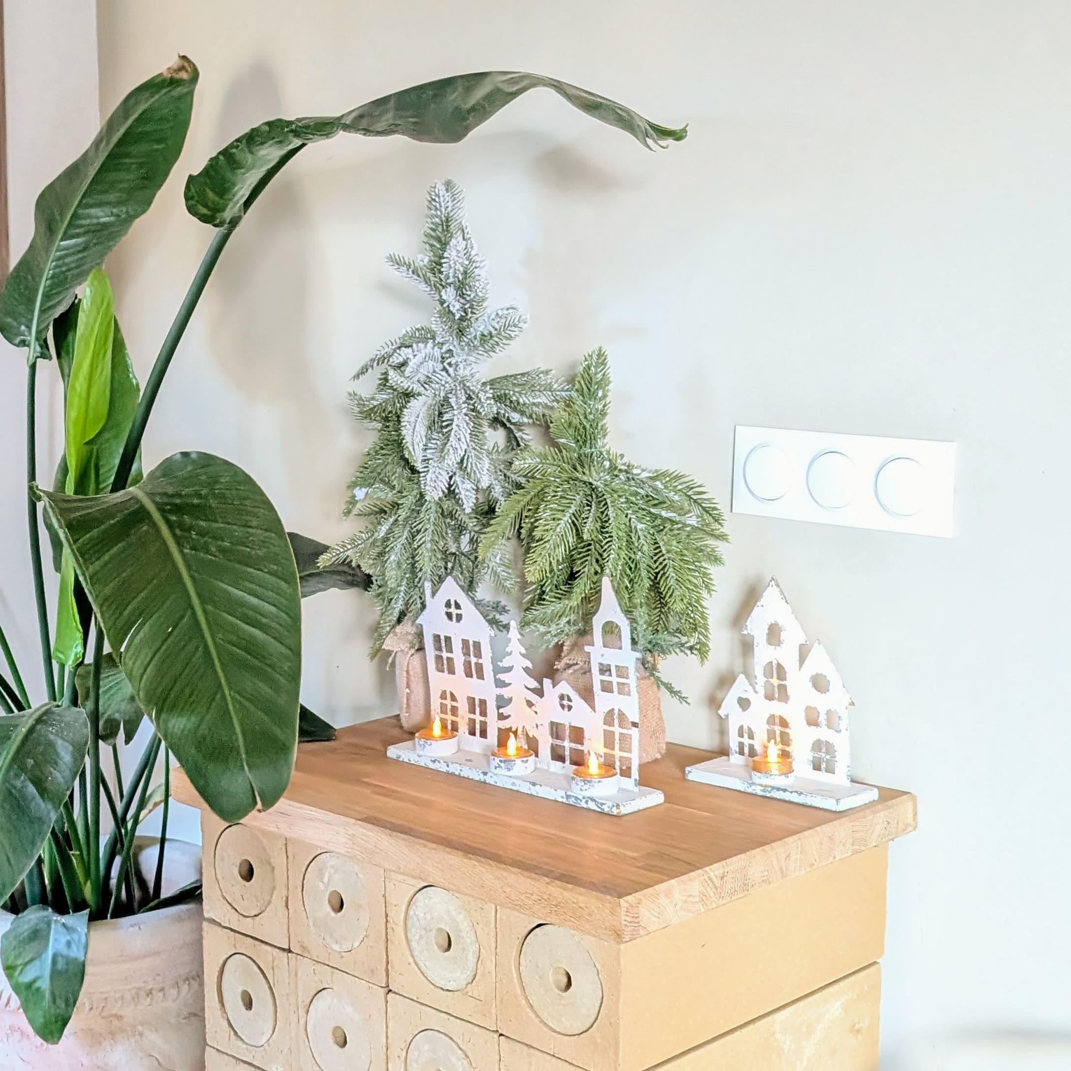 Décoration de Noël avec maisons en bois blanches et bougies chauffe-plat sur table en bois, branches vertes