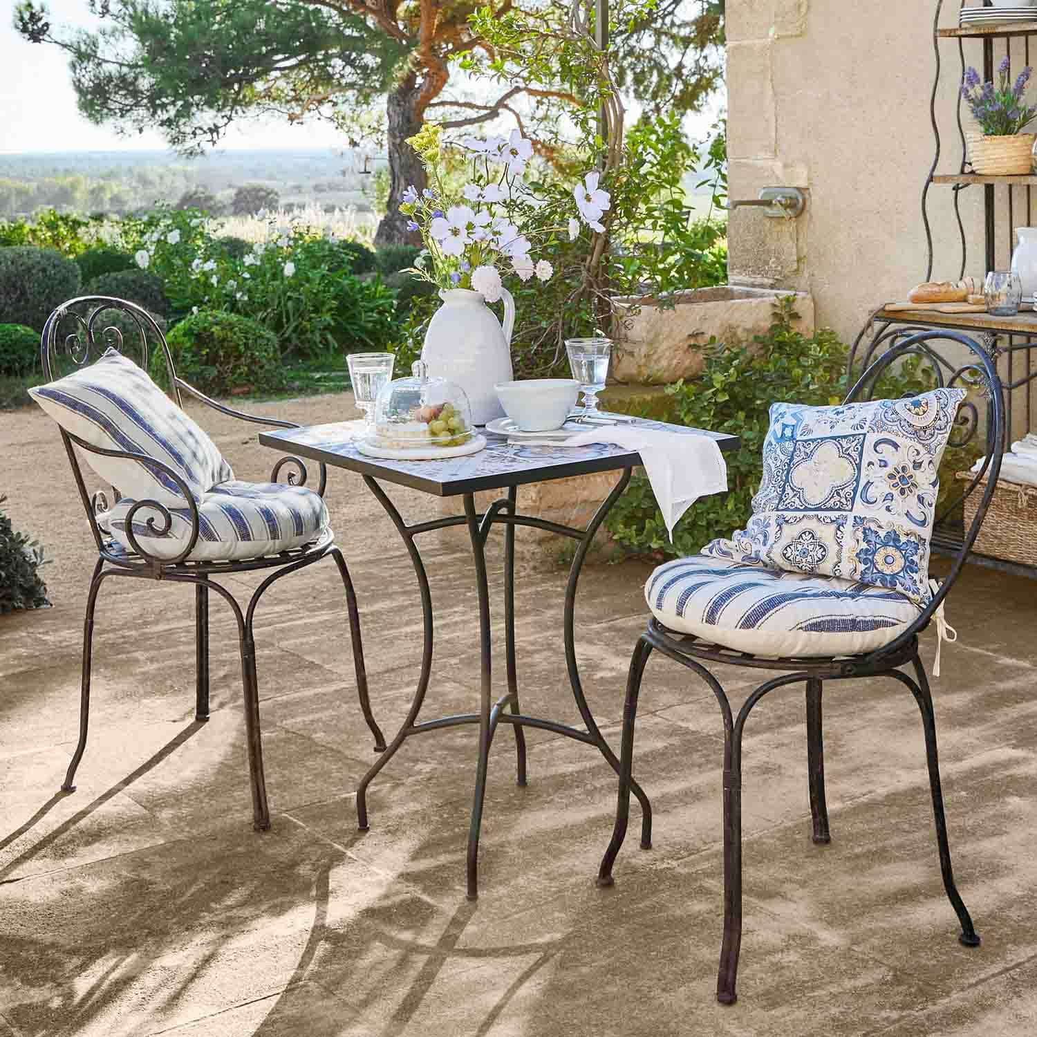Table carrée en métal avec deux chaises aux coussins bleus décoratifs sur terrasse ensoleillée
