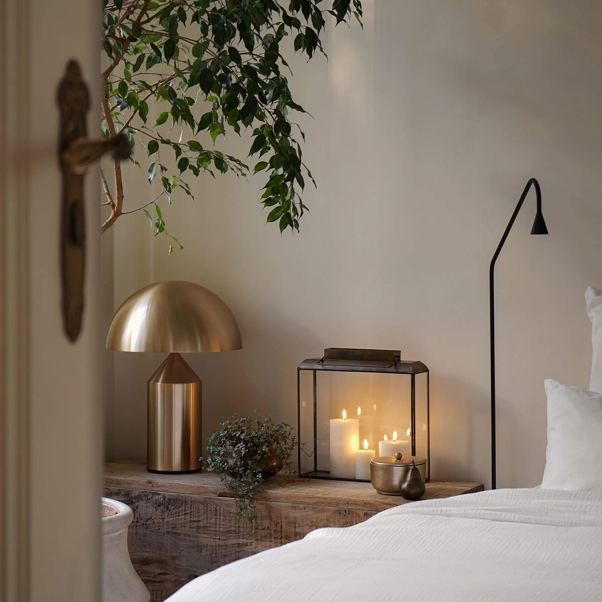 Lampe de table en métal doré et lanterne en verre avec bougies blanches sur table en bois dans une chambre