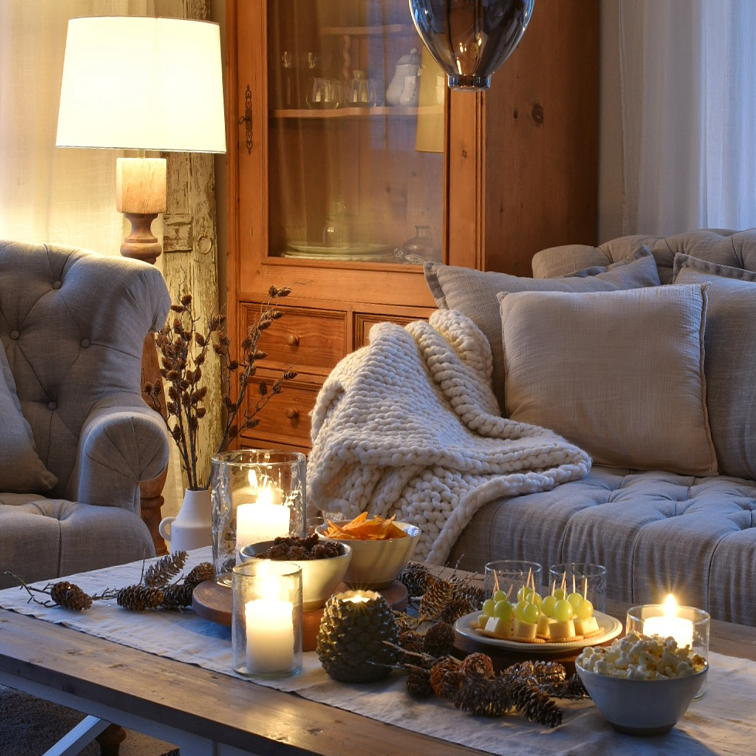 Salon chaleureux avec plaid en tricot beige et table en bois décorée de bougies et amuse-bouches