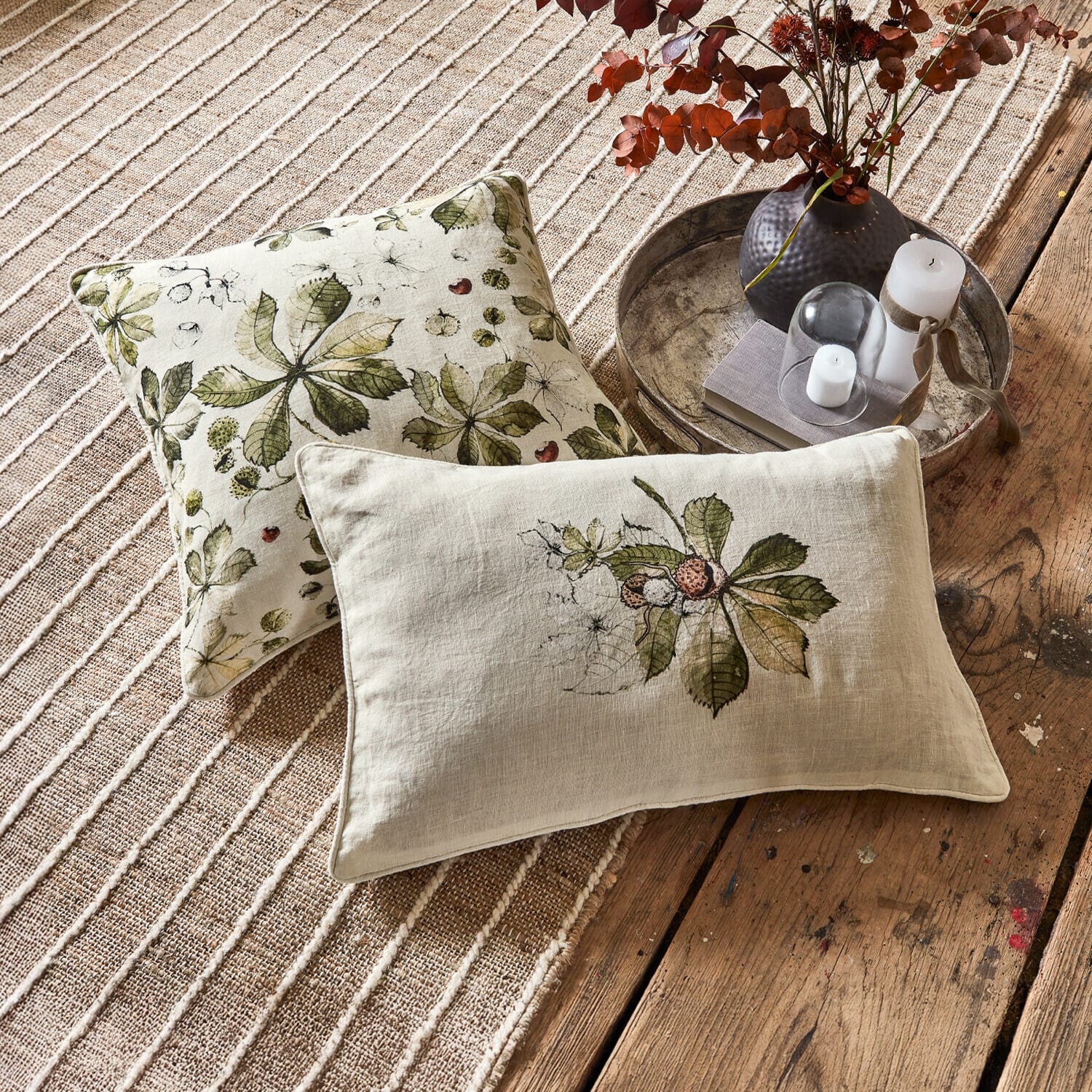 Lot de 2 housses de coussins Elsie Coussins décoratifs en lin avec motifs de feuilles vertes sur fond beige posés sur tapis et plancher en bois