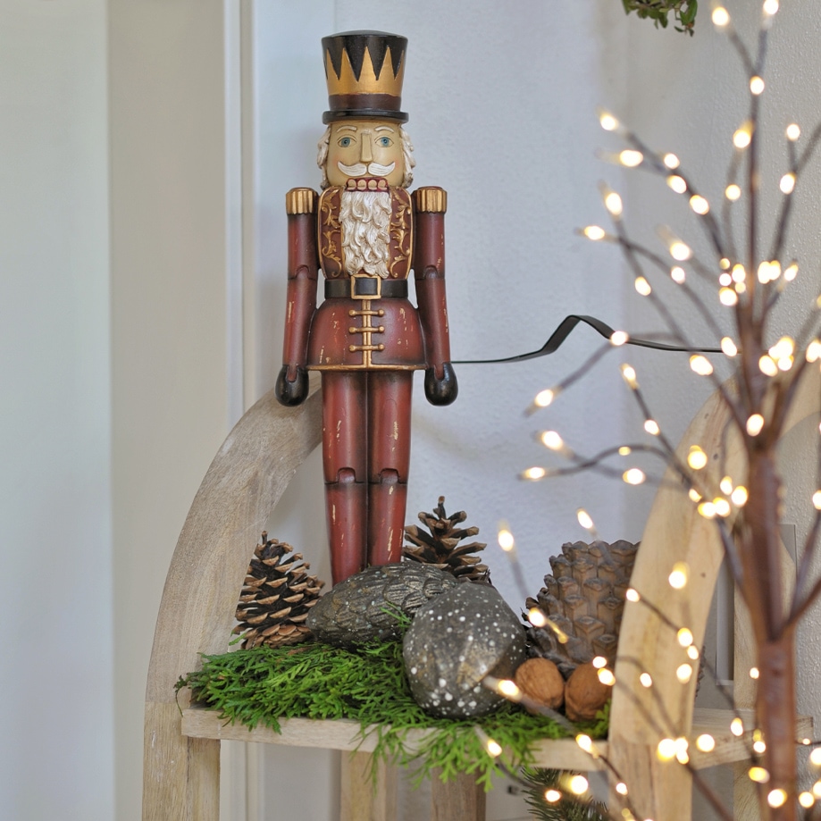 Figurine de casse-noisette rouge en bois avec chapeau noir sur étagère décorative avec branches vertes et pommes de pin