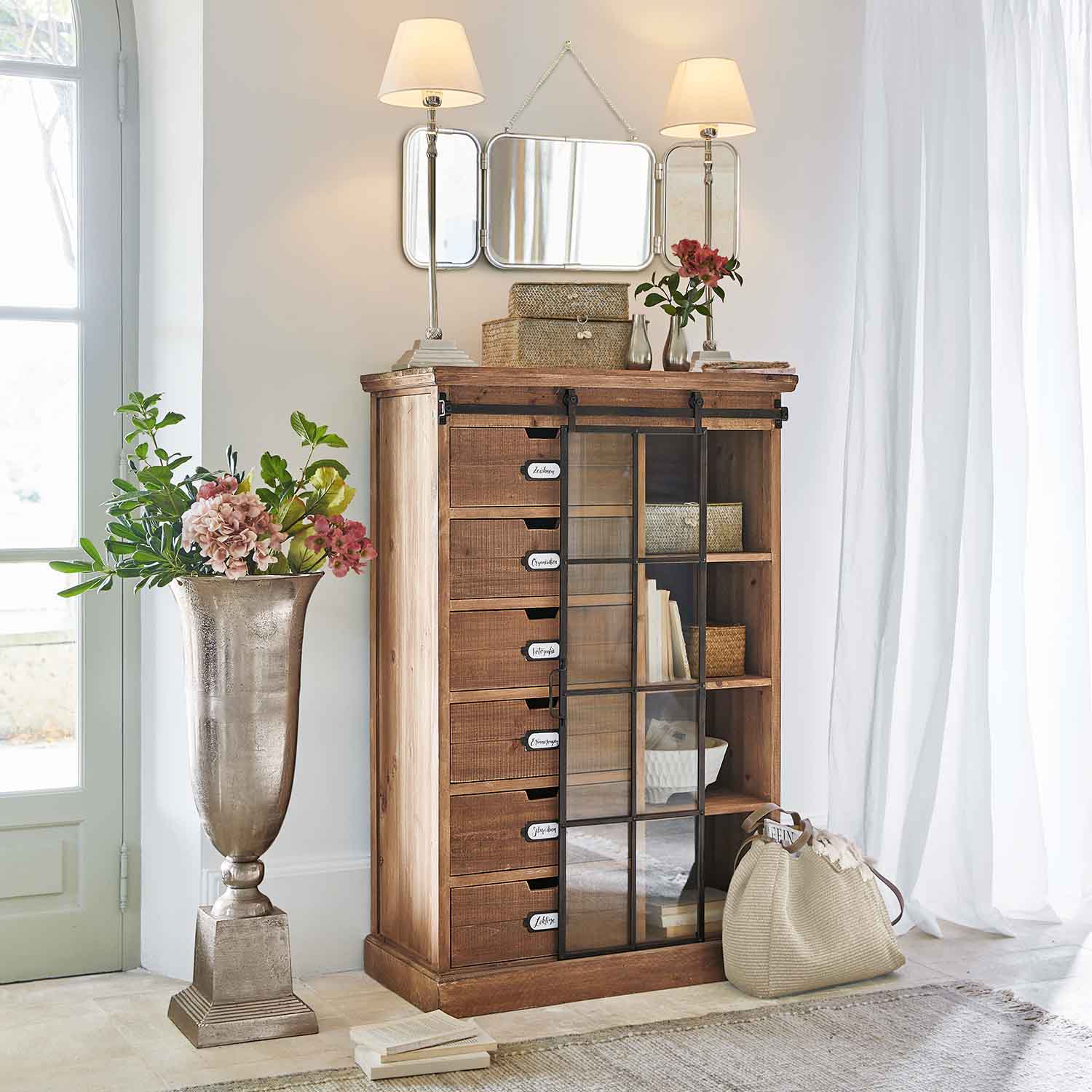 Commode en bois avec tiroirs et porte vitrée dans un intérieur clair avec décorations et lampes