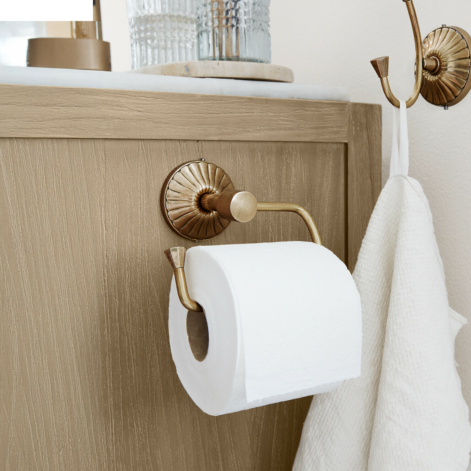 Porte-papier toilette Terling Porte-papier toilette en laiton avec crochet et serviette blanche sur meuble en bois clair