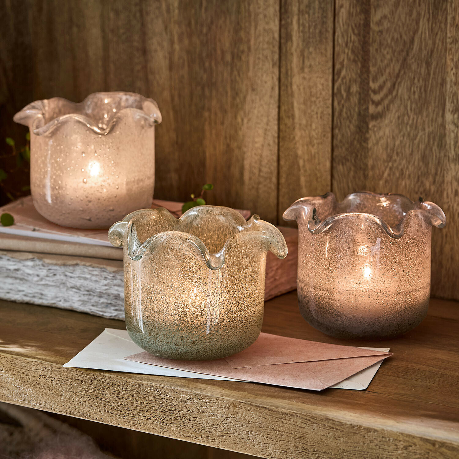 Lot de 3 photophores Venara Trois photophores en verre soufflé aux teintes pastel posés sur une étagère en bois