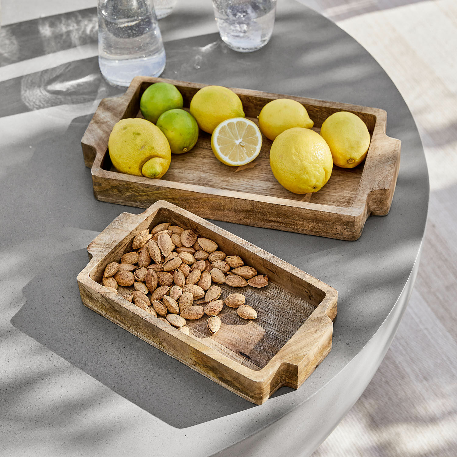 Lot de 2 plateaux Buer Plateaux rectangulaires en bois avec poignées, l'un avec des citrons, l'autre avec des amandes sur table grise