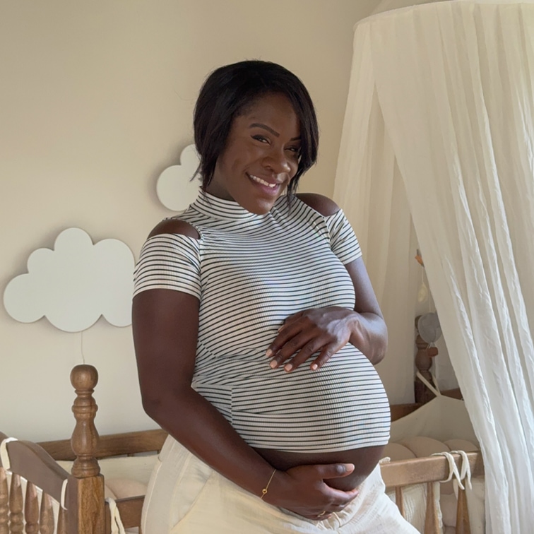 Femme enceinte souriante en haut rayé dans une chambre claire avec un lit bébé en bois