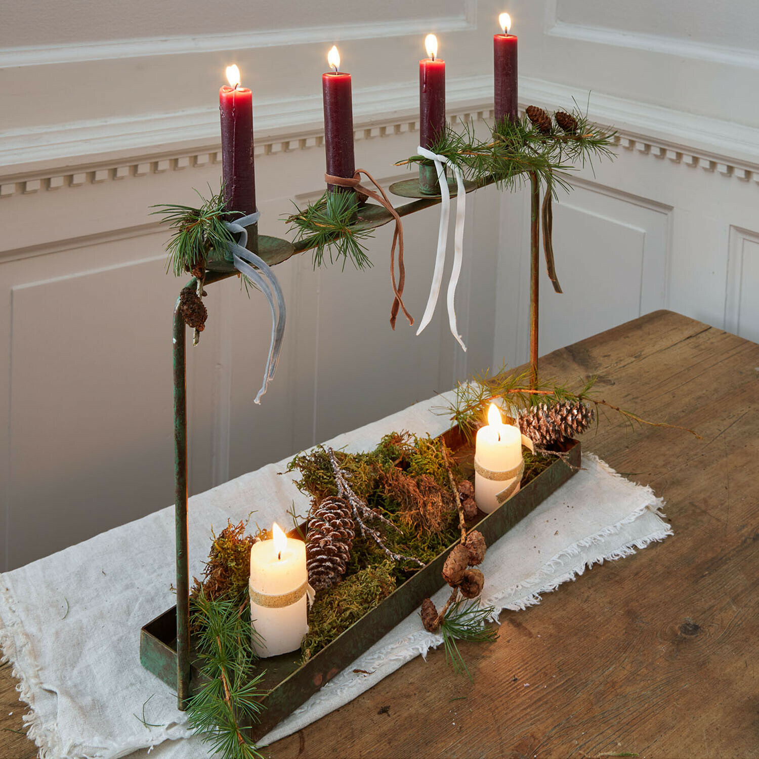 Bougeoir Valenzas Chandelier en métal avec quatre bougies rouges et décorations de pommes de pin et branches vertes sur table en bois
