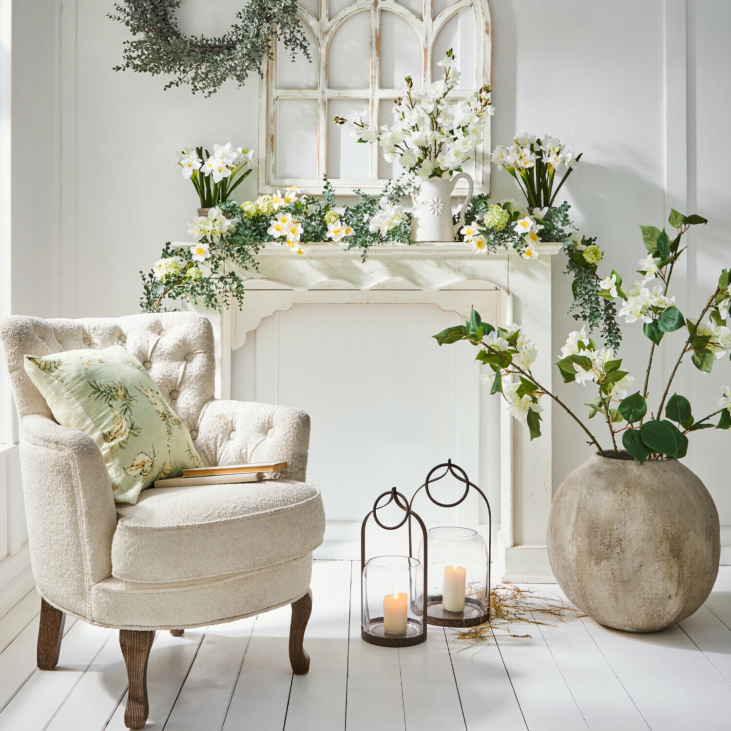 Manteau de cheminée Claybourne Fauteuil crème confortable avec pieds en bois près d'une cheminée décorée de fleurs blanches et bougies