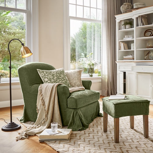 Fauteuil vert en tissu avec repose-pieds et plaid beige dans un salon lumineux avec grande fenêtre