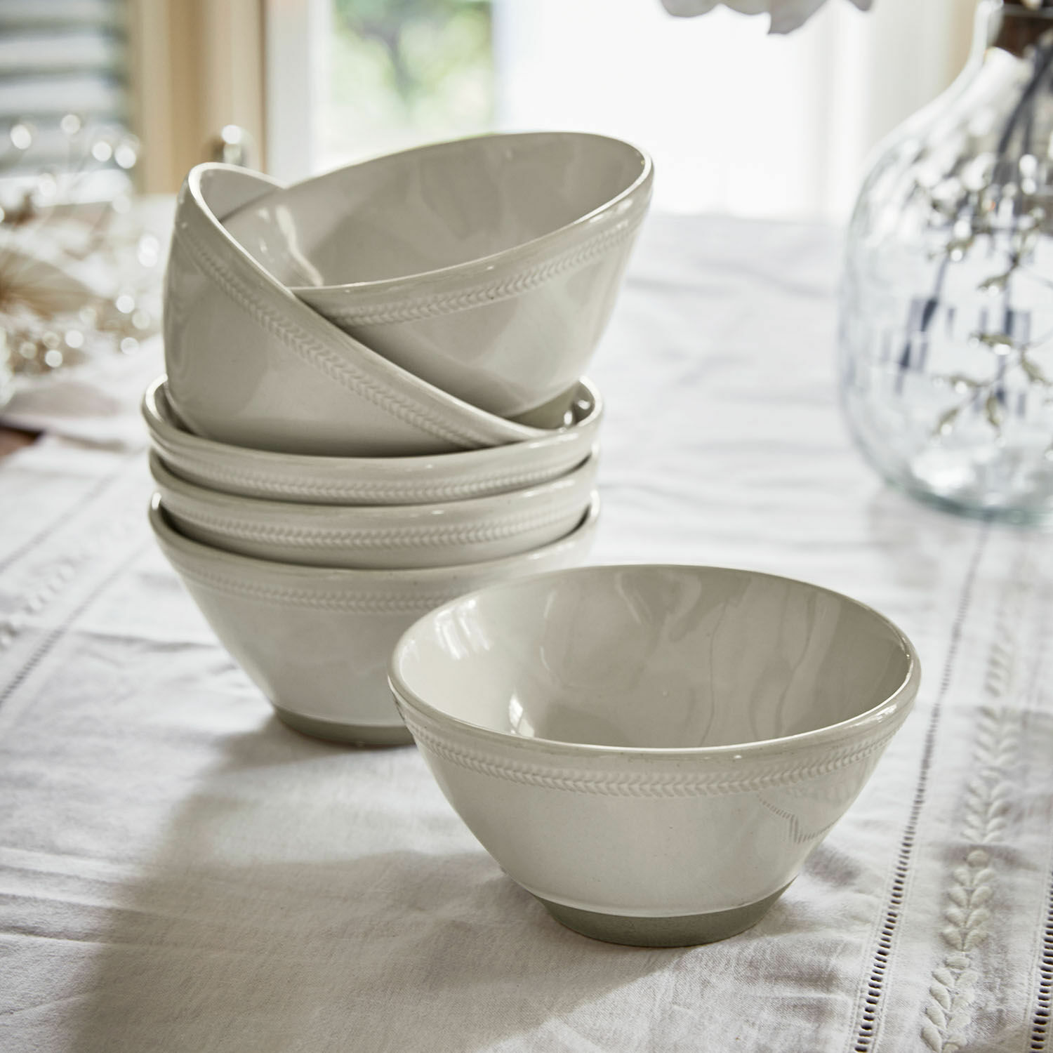 Ensemble de bols en céramique blanche avec motif discret sur le bord, posés sur une nappe