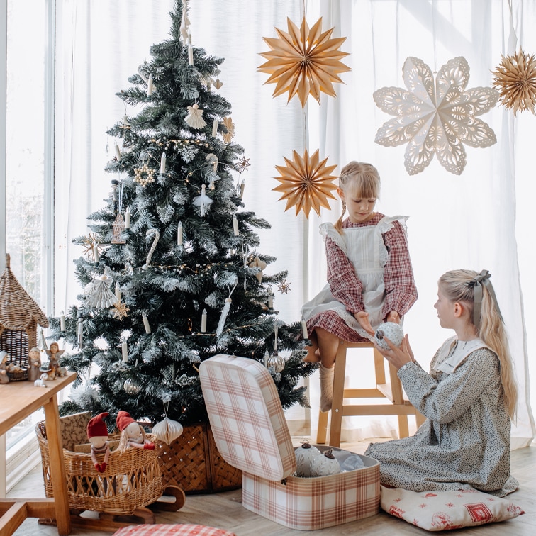 Enfants près d'un sapin décoré avec des ornements naturels et des étoiles en papier dans une pièce lumineuse