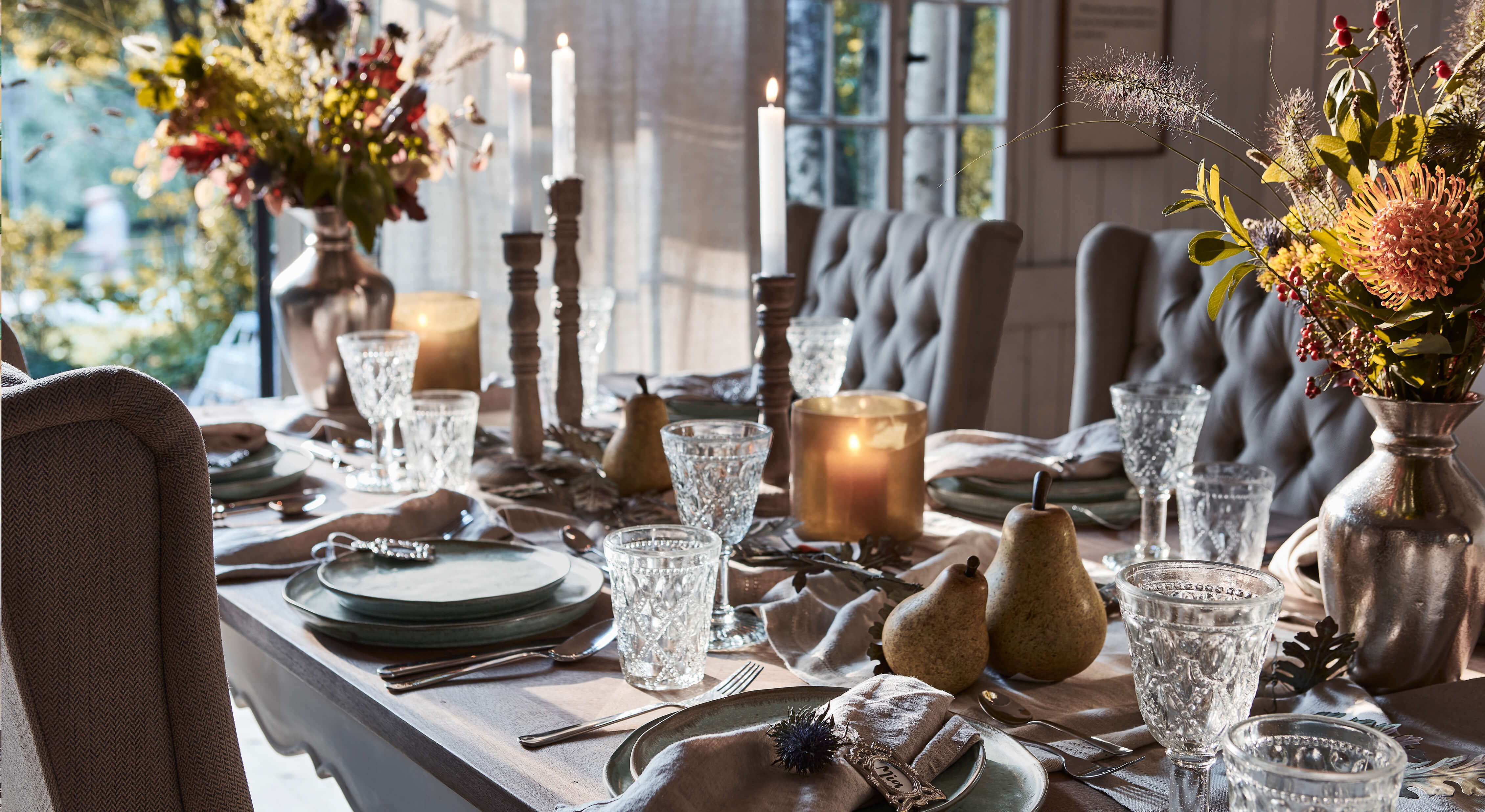 Table élégamment dressée avec assiettes grises, verres en cristal et bougies dans un intérieur chaleureux