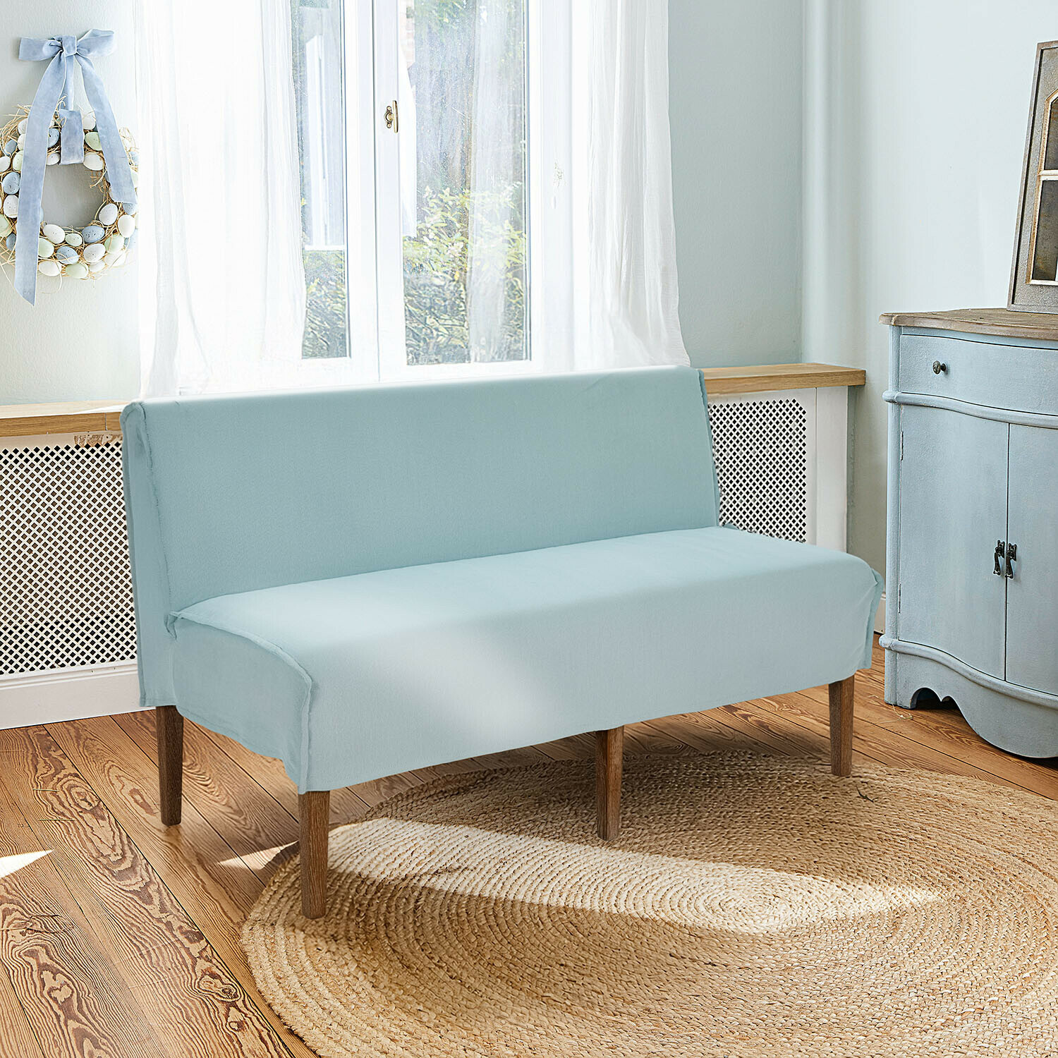 Banquette de cuisine Vinterfjord Housse de canapé en coton bleu clair avec pieds en bois dans un salon lumineux avec tapis en jute