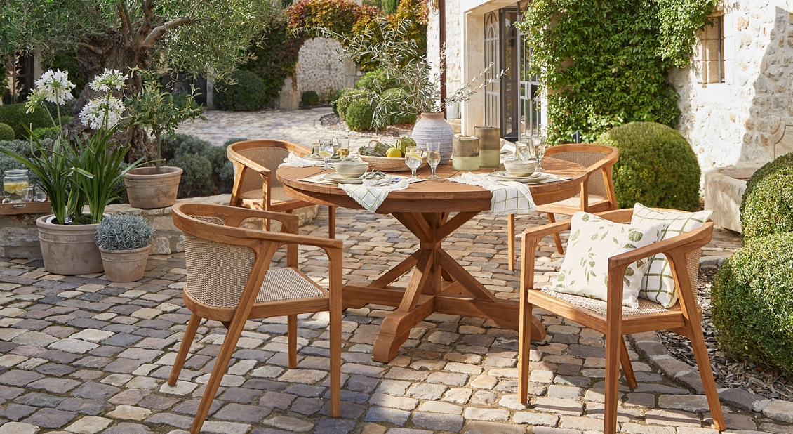 Table ronde en bois avec quatre chaises sur pavés dans une cour ensoleillée décorée de plantes