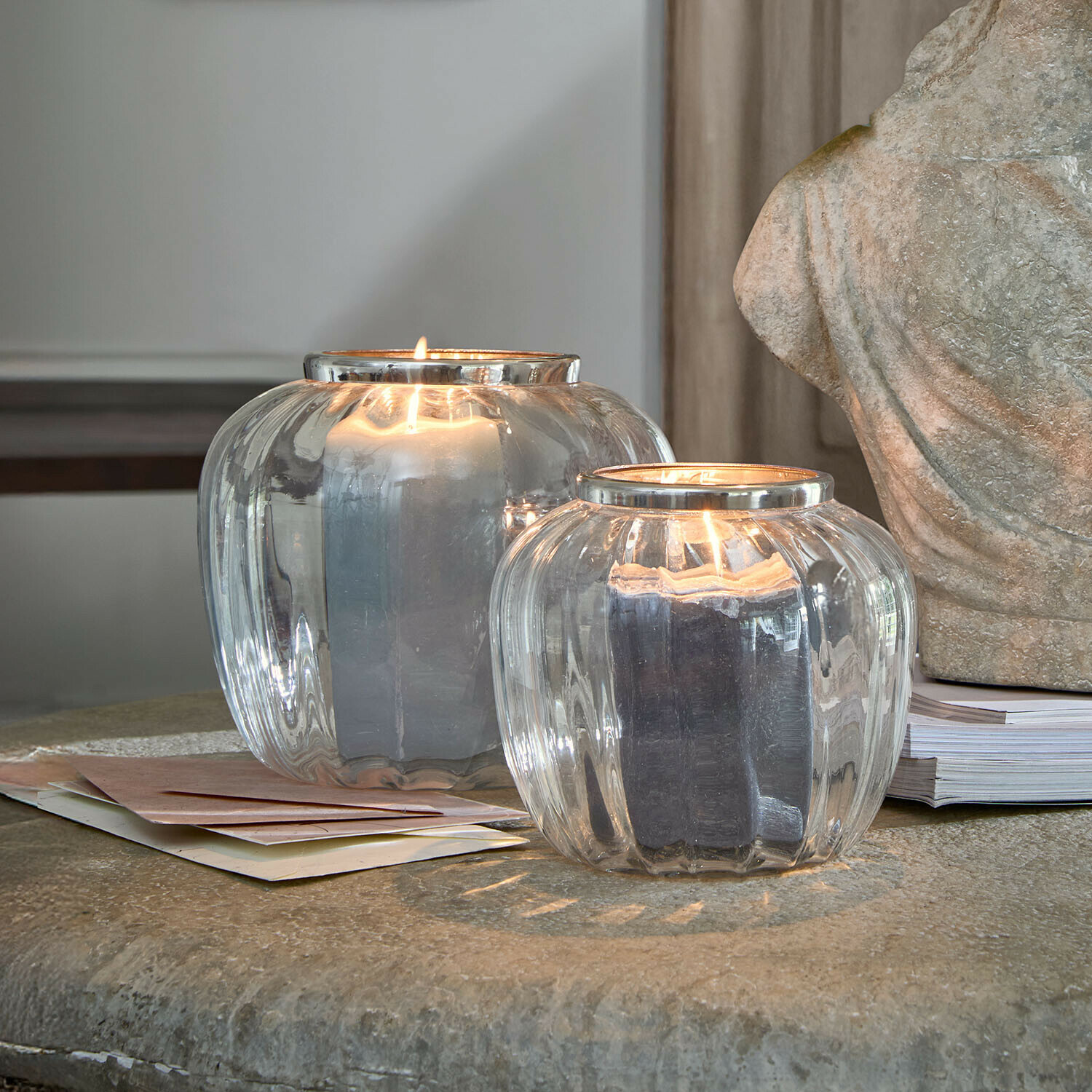 Lot de 2 photophores Fioren Deux photophores en verre transparent avec bougies noires allumées sur une table en pierre