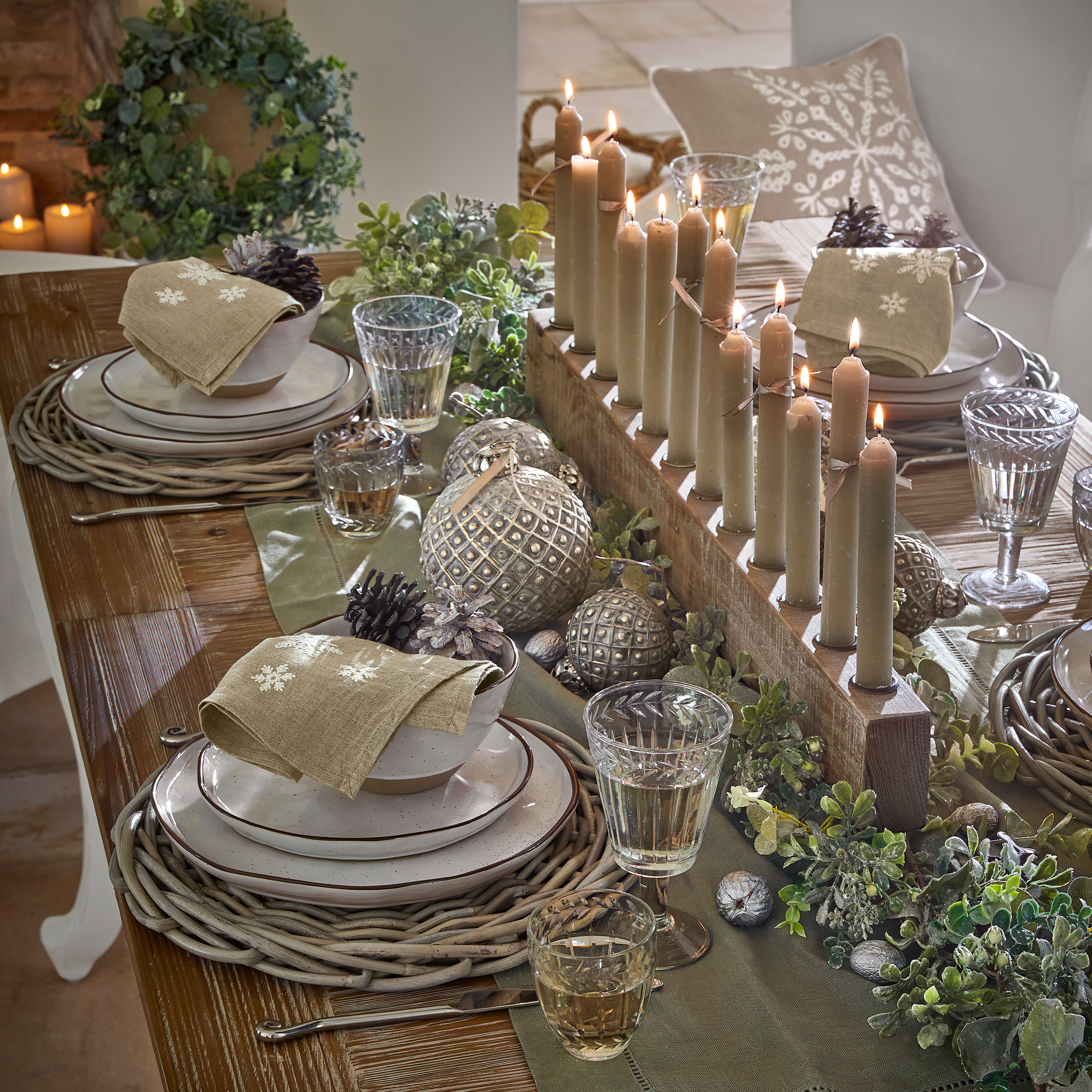 Table en bois rustique décorée de bougies, verdure et vaisselle aux tons naturels pour une ambiance chaleureuse