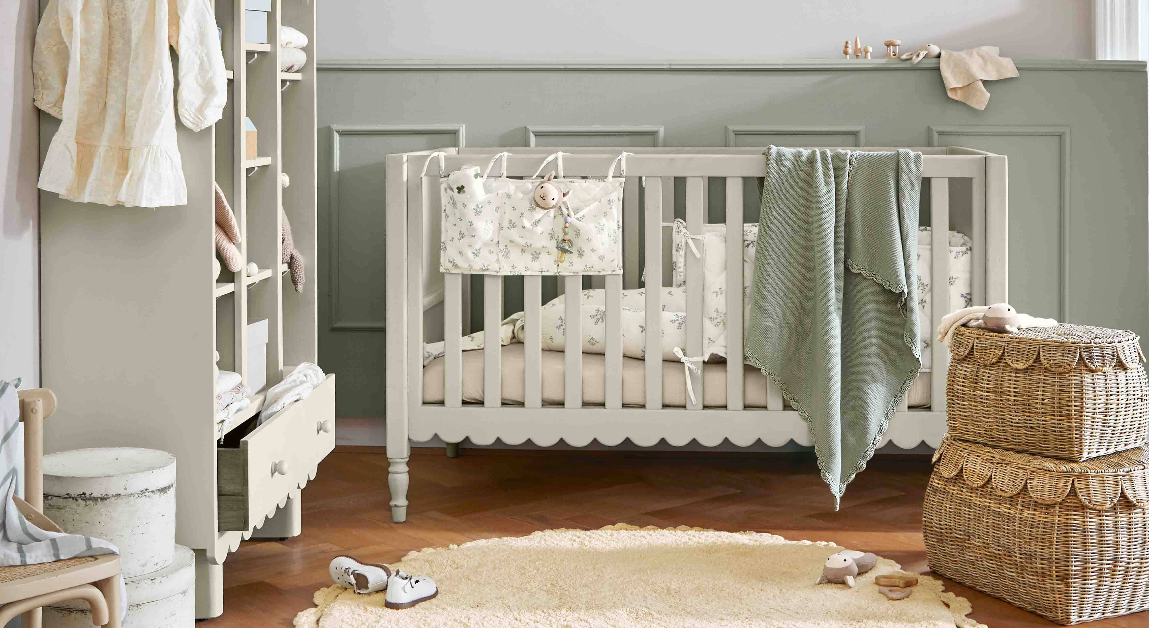 Lit bébé en bois gris avec couverture verte et paniers en osier dans une chambre d'enfant chaleureuse