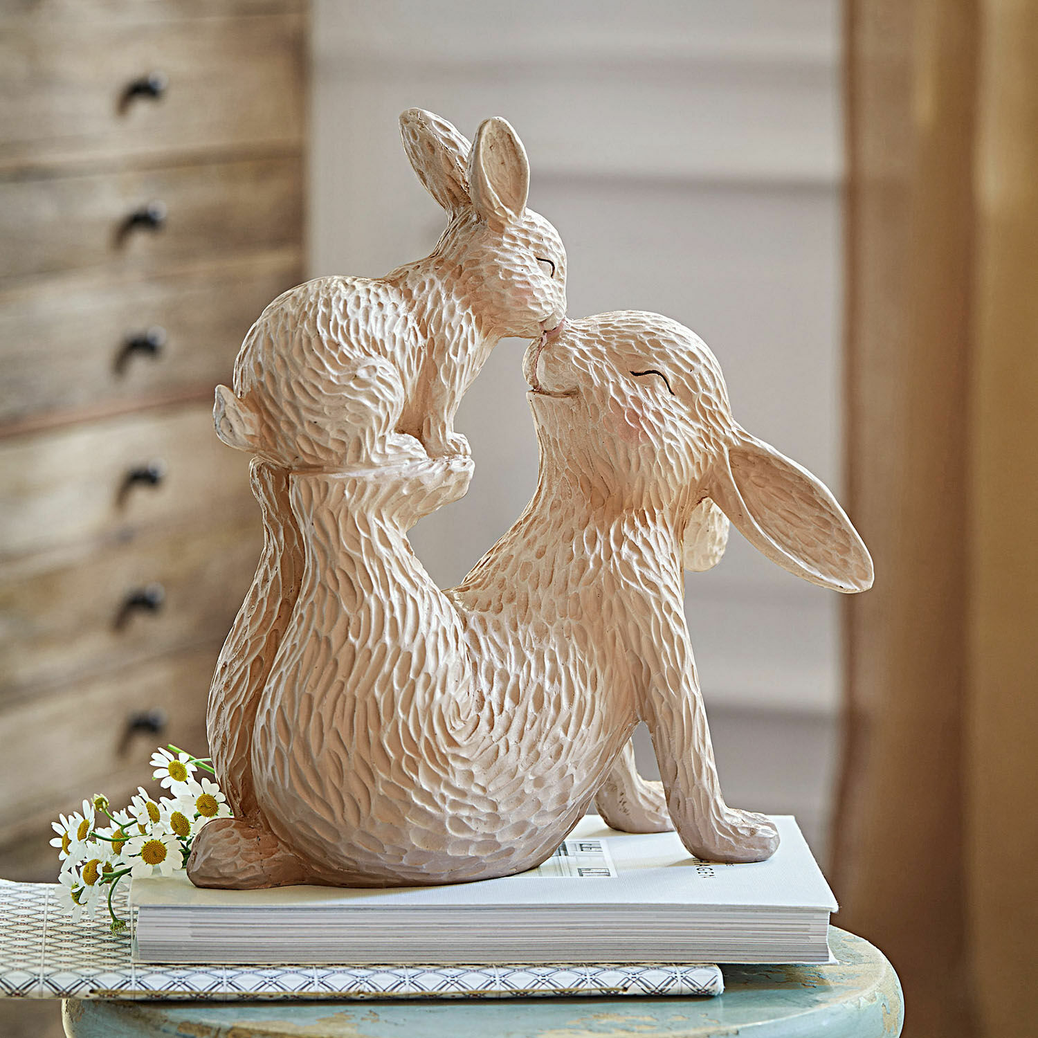 Lapins décoratifs Trista Figurine beige en céramique de deux lapins dans une pose ludique sur une table avec des livres