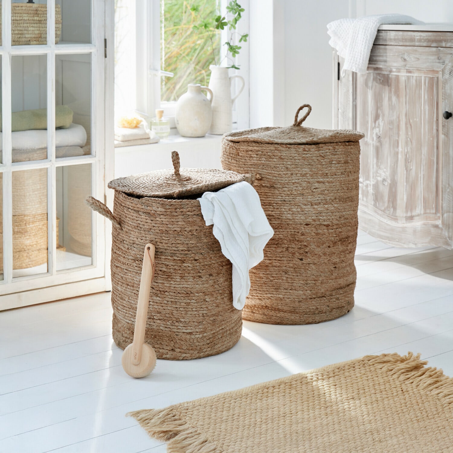 Lot de 2 paniers à linge Kory Deux paniers à linge ronds en jute naturelle beige dans une salle de bain lumineuse