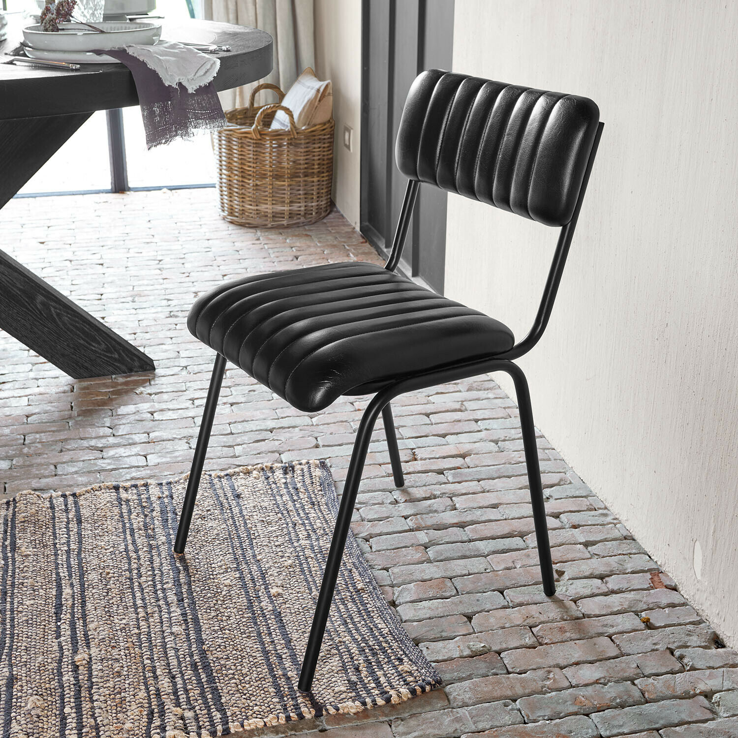 Chaise Jolivon Chaise noire avec assise et dossier en cuir matelassé sur cadre métallique dans une pièce au sol en briques