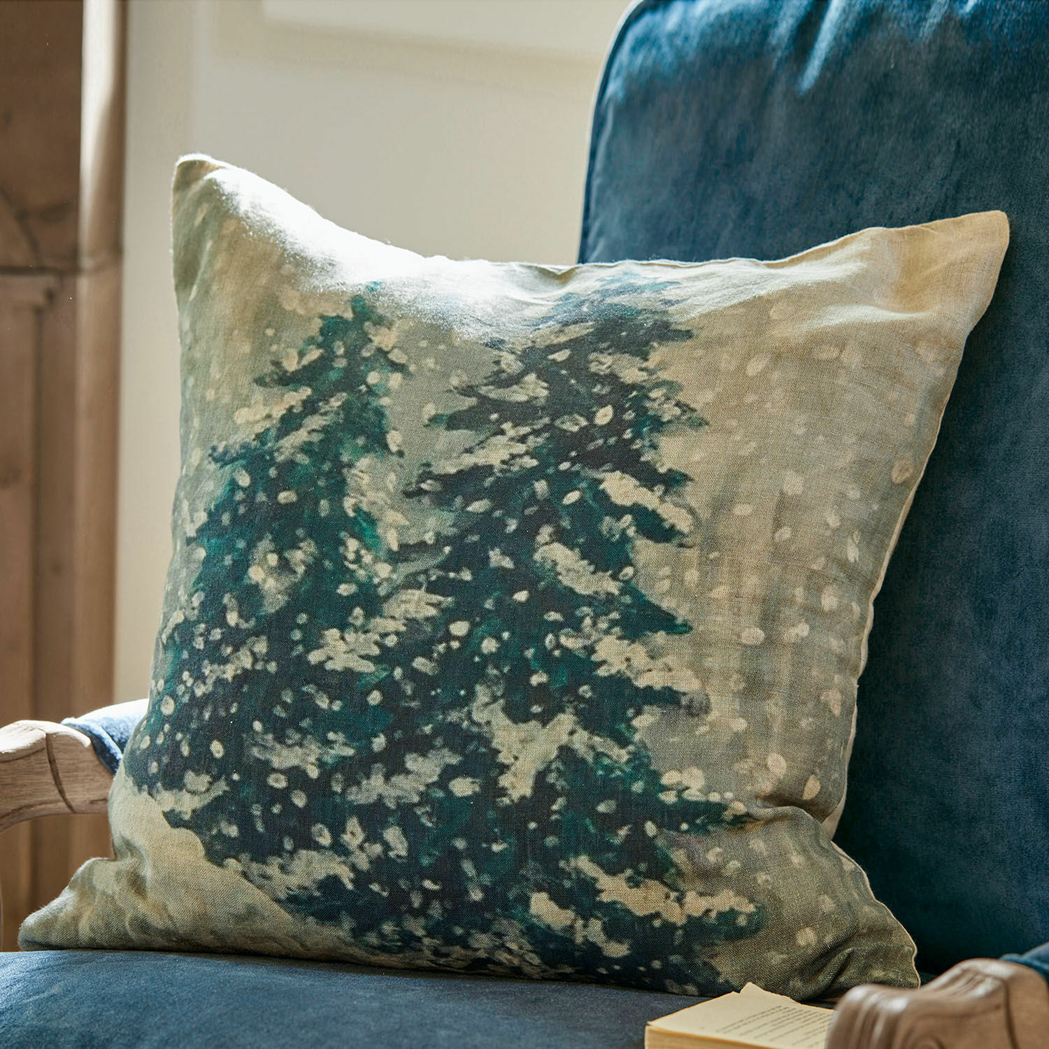 Housse de coussin Mierta Coussin décoratif en lin avec motif sapins verts sur fond beige posé sur un fauteuil bleu