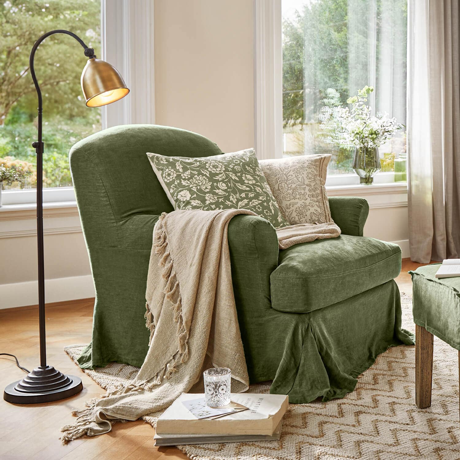 Fauteuil vert en tissu avec couverture beige et coussins à motifs floraux dans un salon lumineux