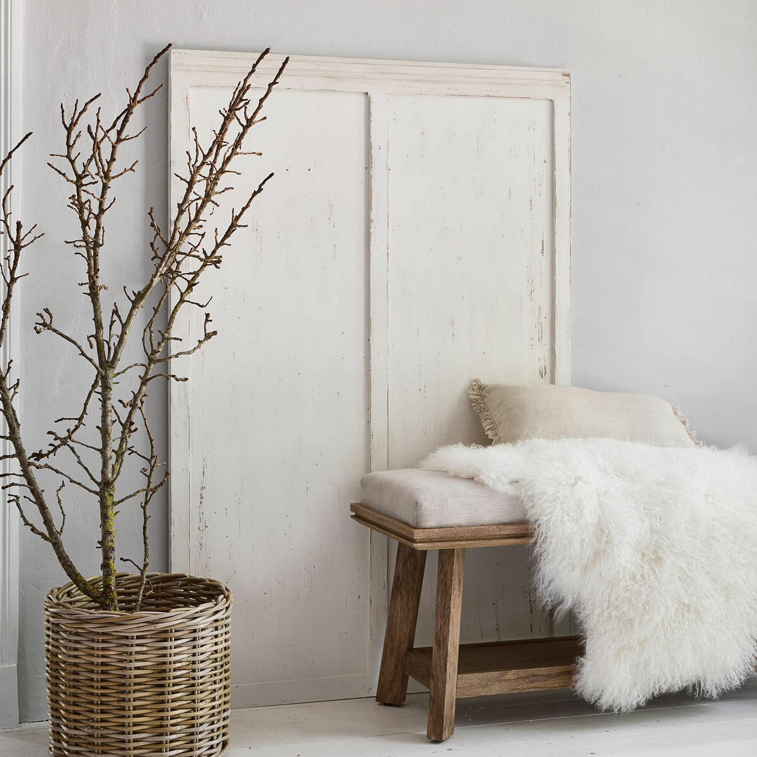 Panneau Evanston Banc en bois avec coussin beige et couverture en fausse fourrure blanche à côté d'un panier en osier avec branches