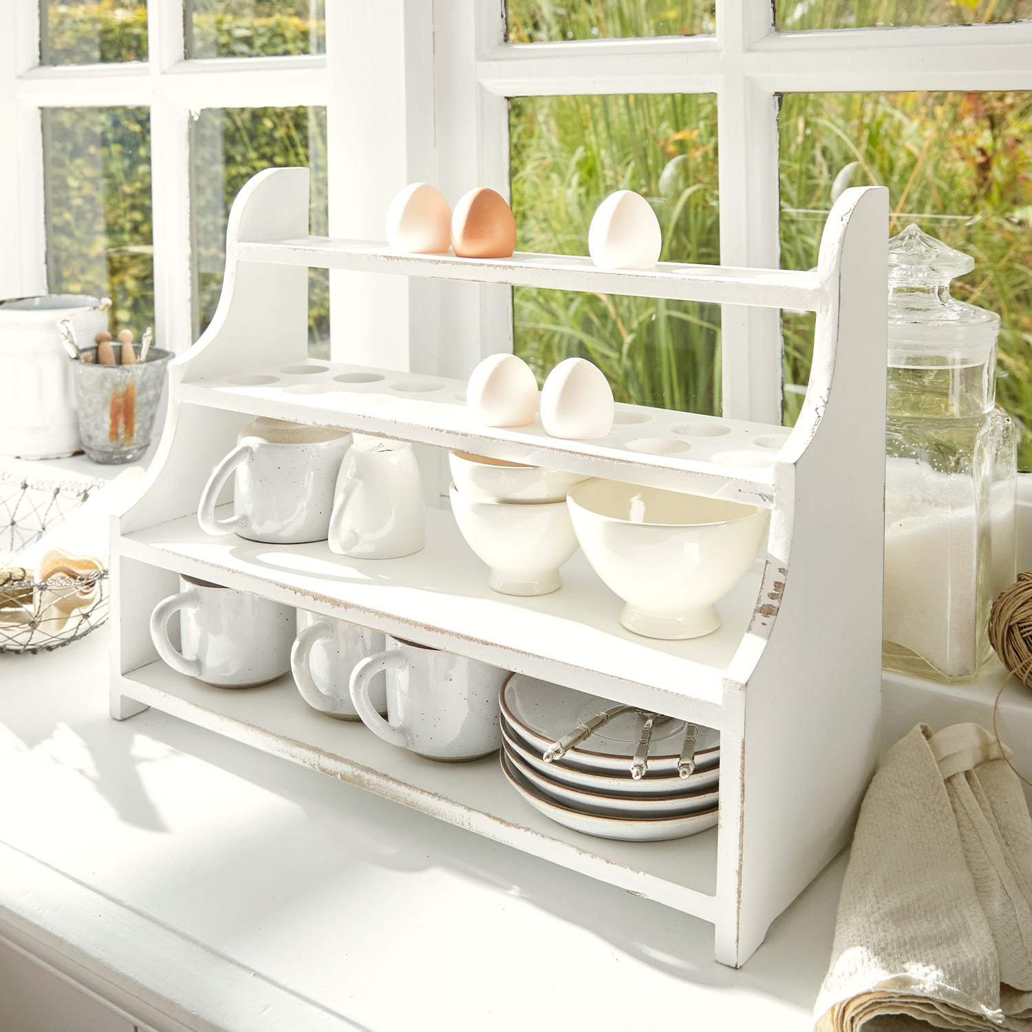Étagère de cuisine en bois blanc avec emplacements pour œufs, tasses et bols dans une cuisine lumineuse