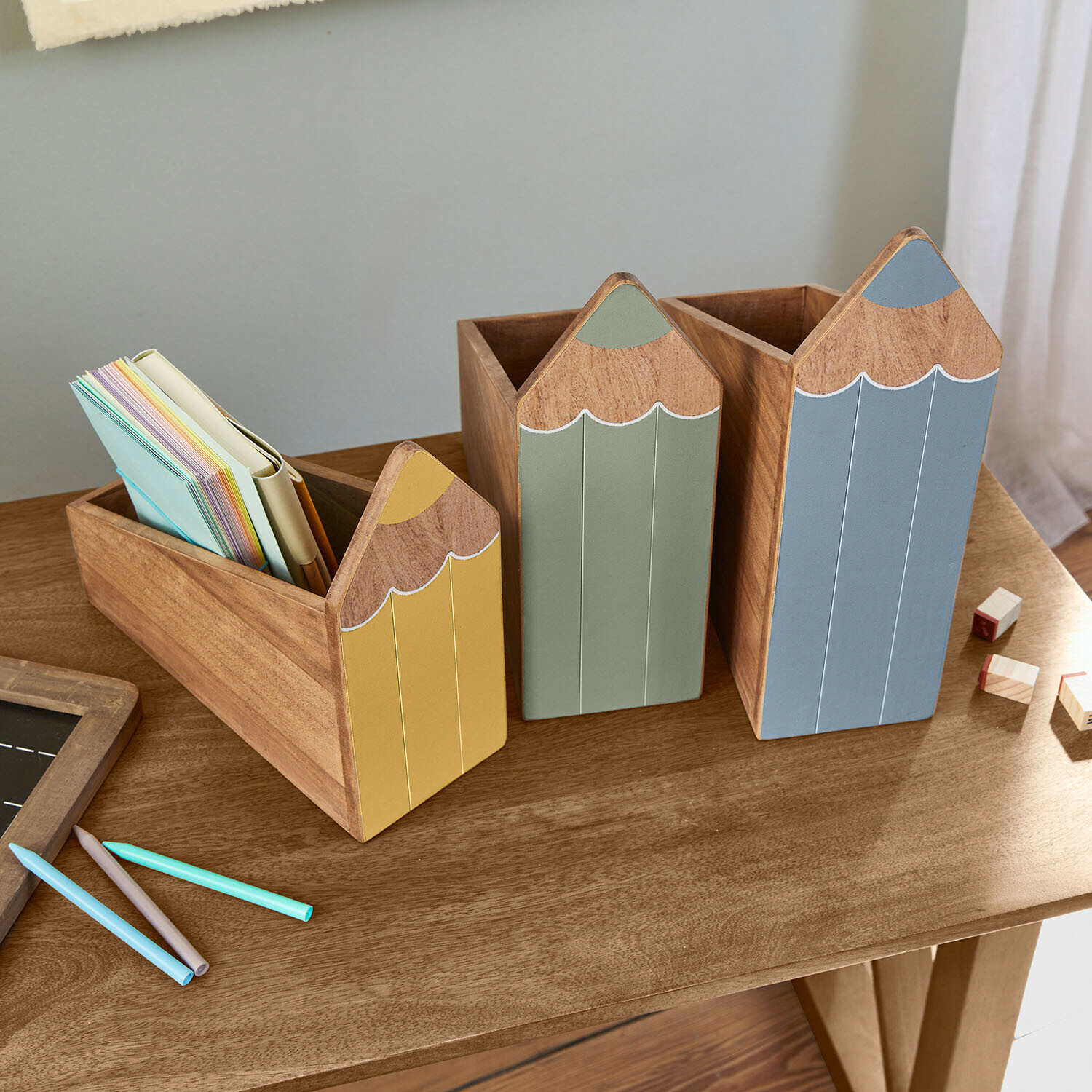 Lot de 3 rangements Sønvik Ensemble de trois organiseurs en bois en forme de crayons jaunes, verts et bleus sur un bureau en bois