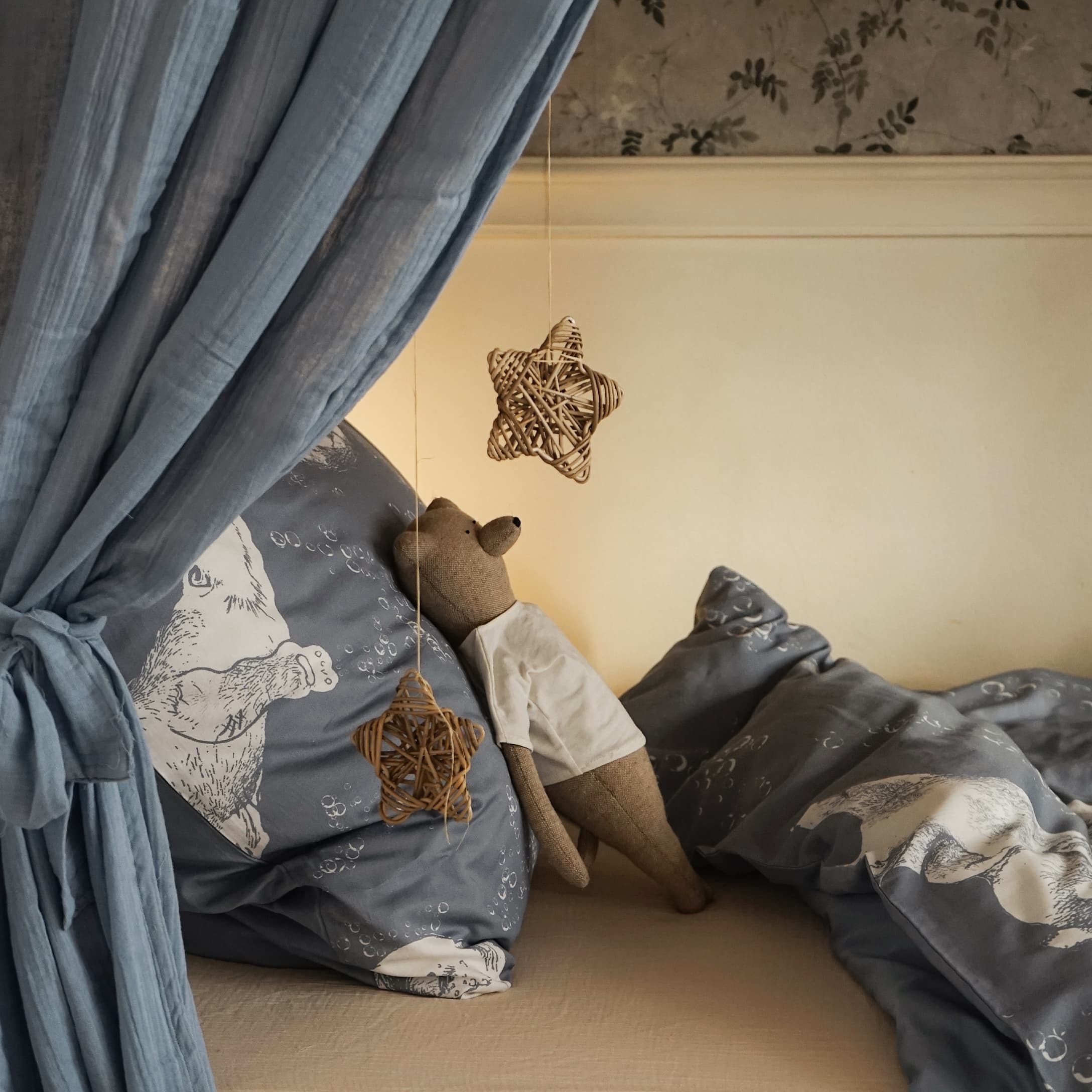 Linge de lit gris avec motif ours et peluche ours en t-shirt blanc sur lit avec rideau bleu