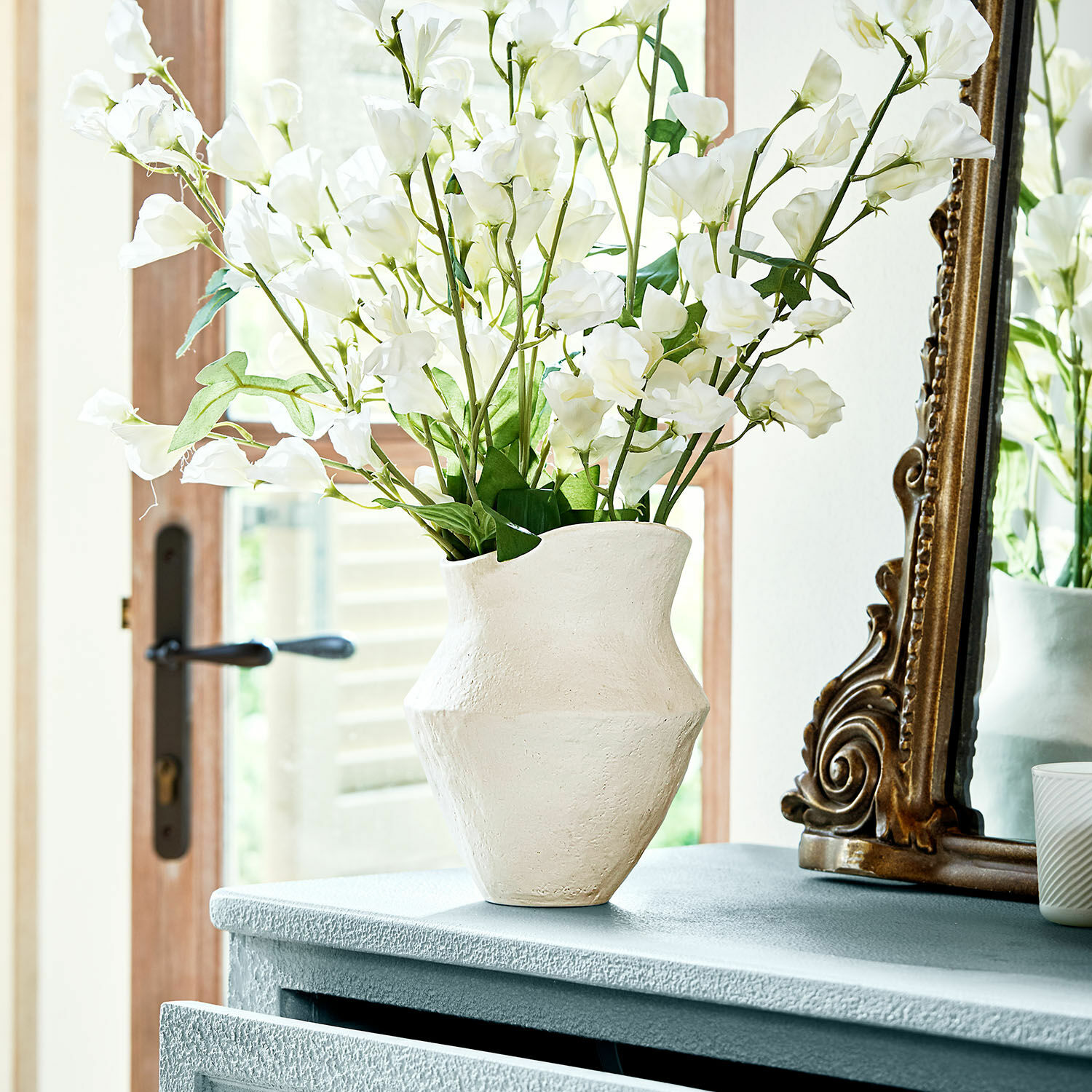 Vase Cantresse Vase en céramique blanche texturée sur commode avec fleurs décoratives dans une pièce lumineuse