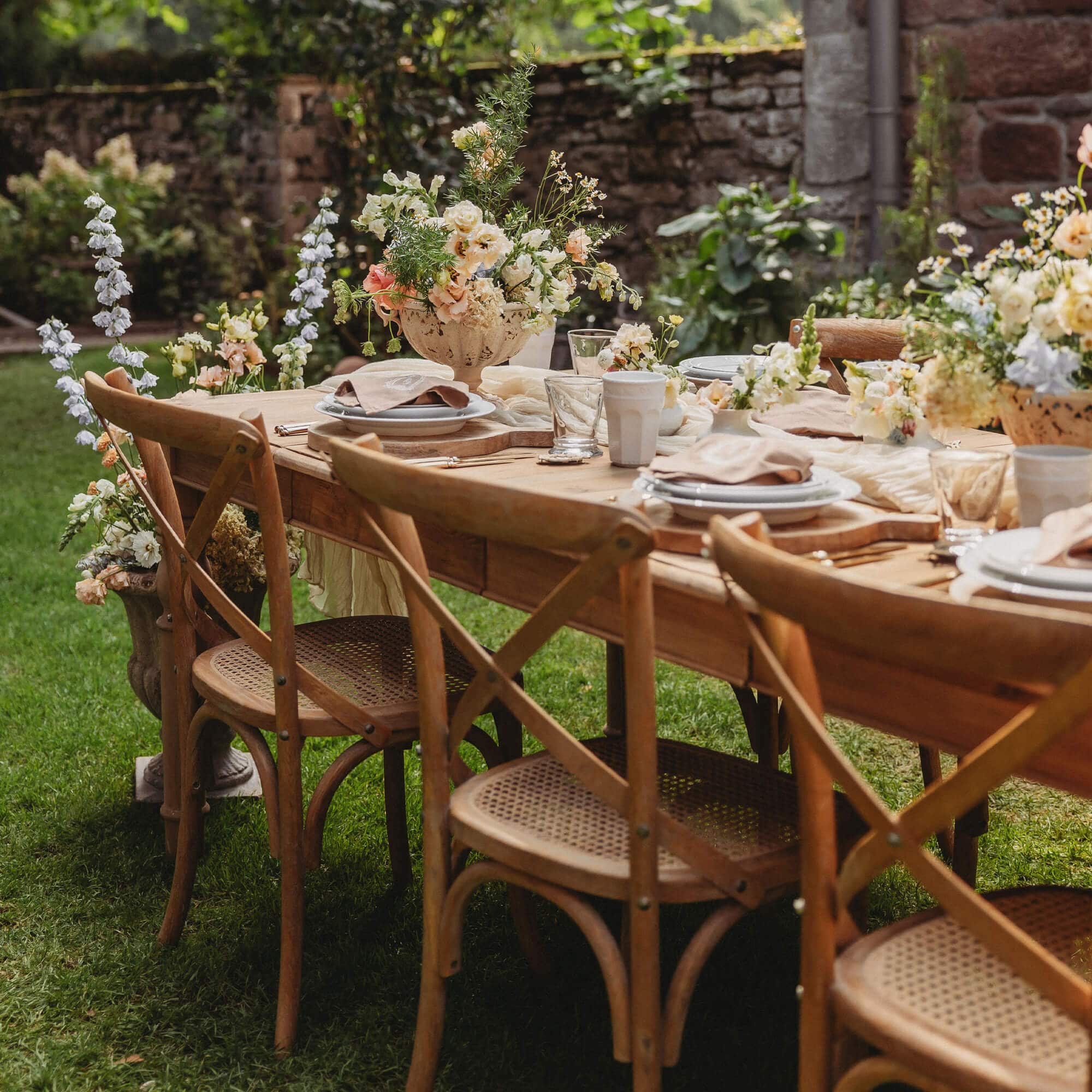 Table de jardin en bois avec chaises en osier et décorations florales sur pelouse verte