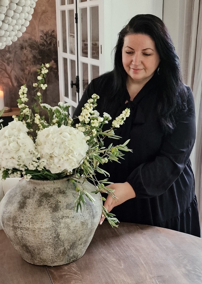 Grand vase en pierre avec fleurs blanches sur table en bois dans un intérieur chaleureux avec femme en robe noire