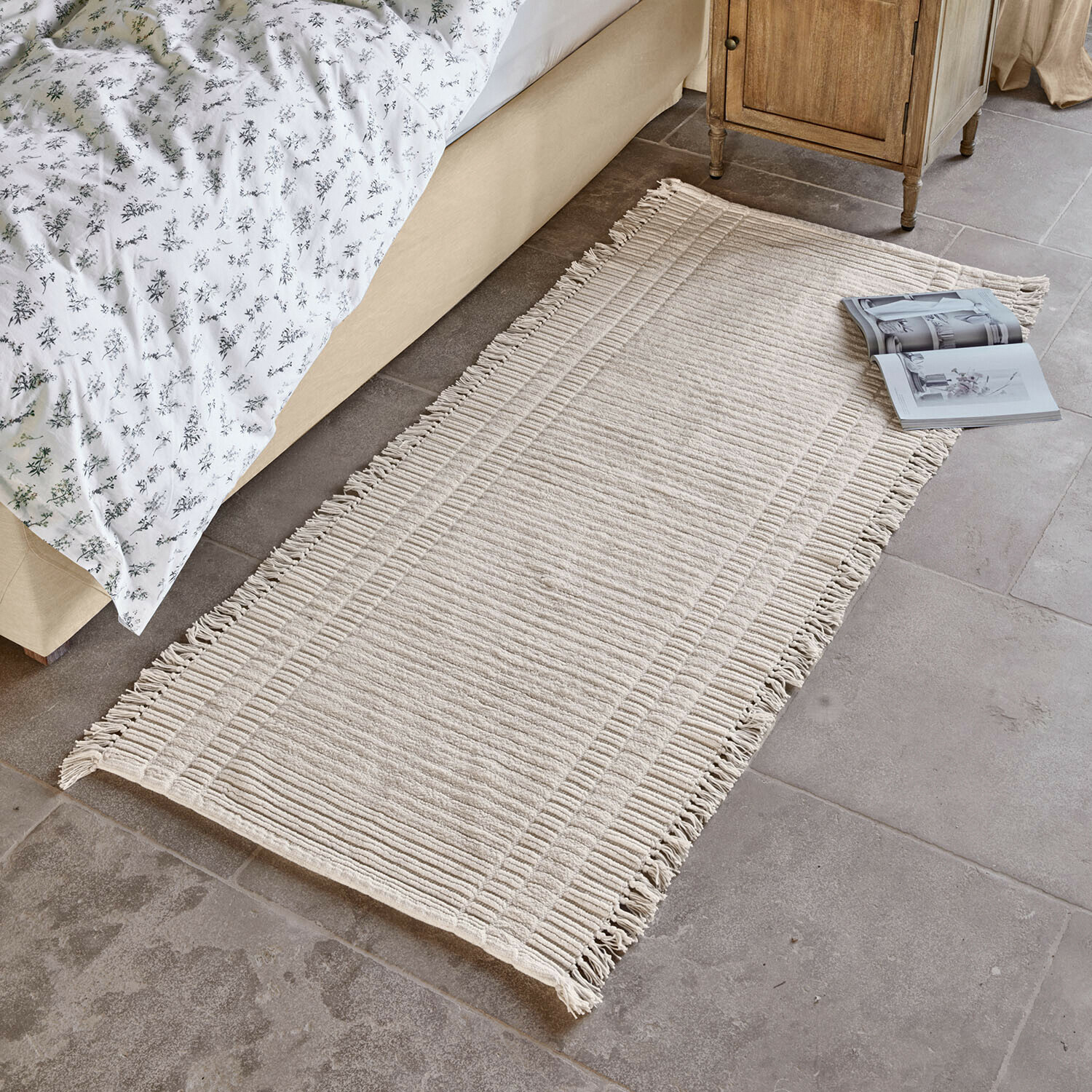 Tapis long Clairenne Tapis beige en coton avec franges posé au sol près d'un lit et d'une table de chevet en bois