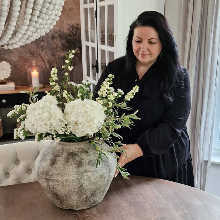 Grand vase en céramique grise avec fleurs blanches sur table en bois dans un intérieur chaleureux.