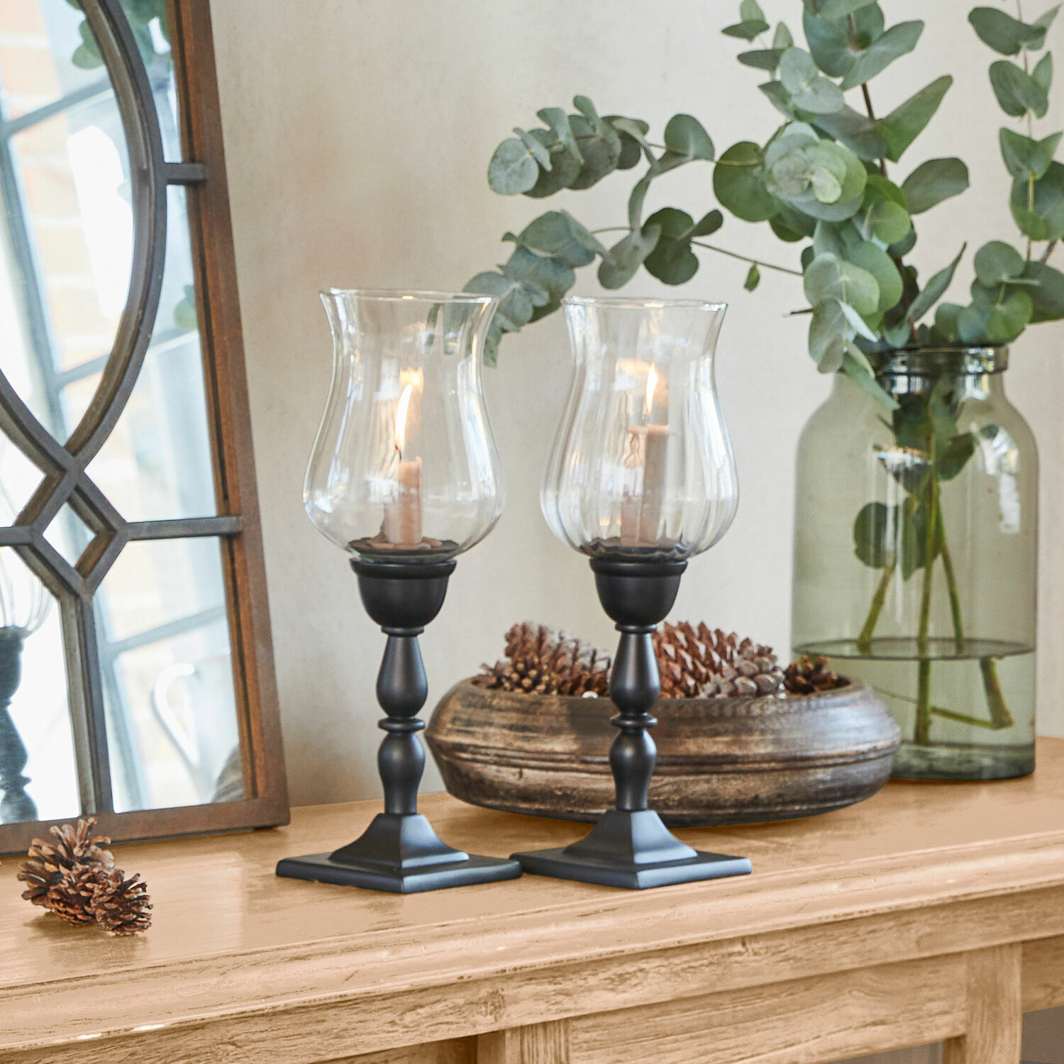 Lot de 2 photophores Monteria Paire de bougeoirs noirs avec verre transparent sur table en bois décorée de pommes de pin