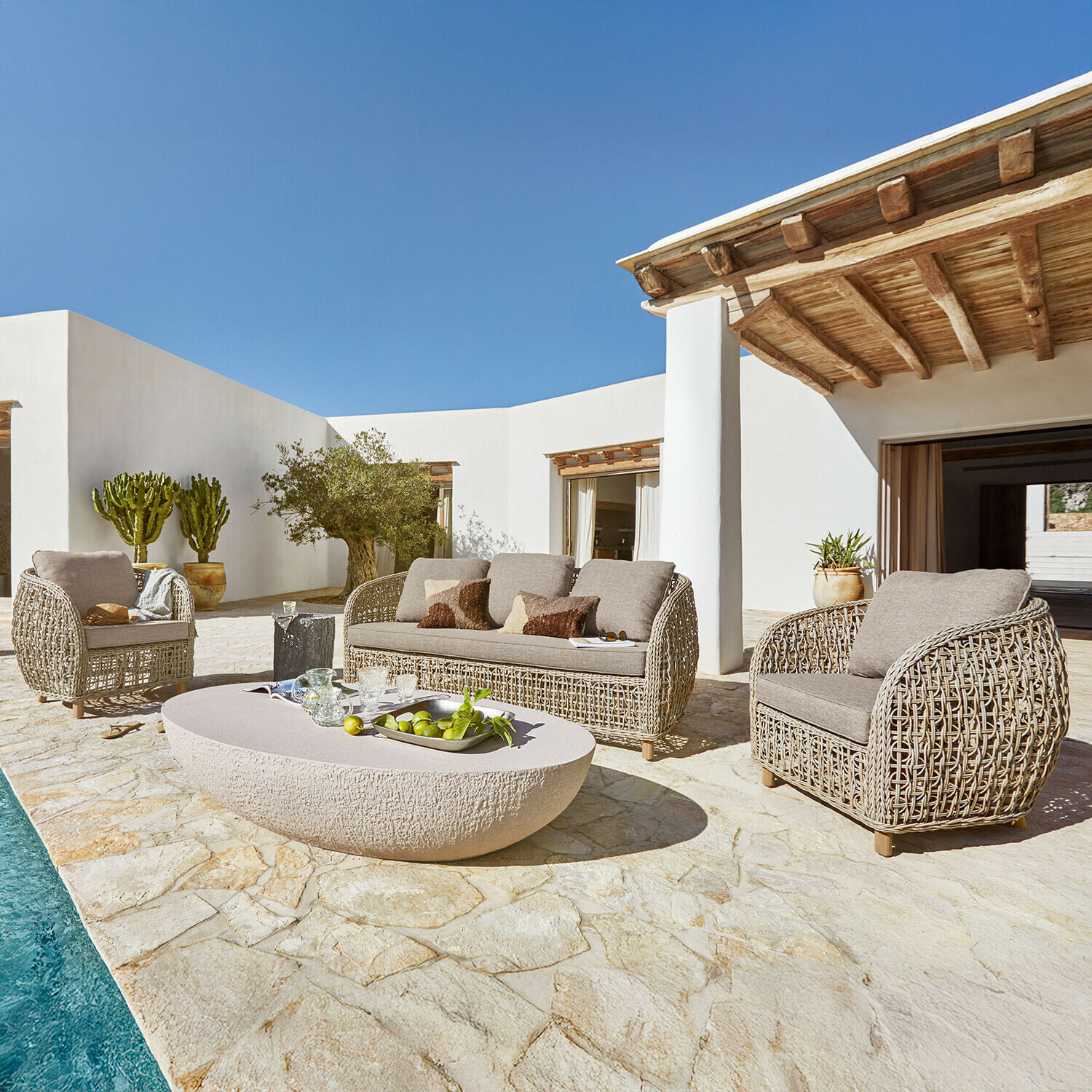 Ensemble de mobilier de jardin en rotin beige avec coussins sur terrasse en pierre près de la piscine