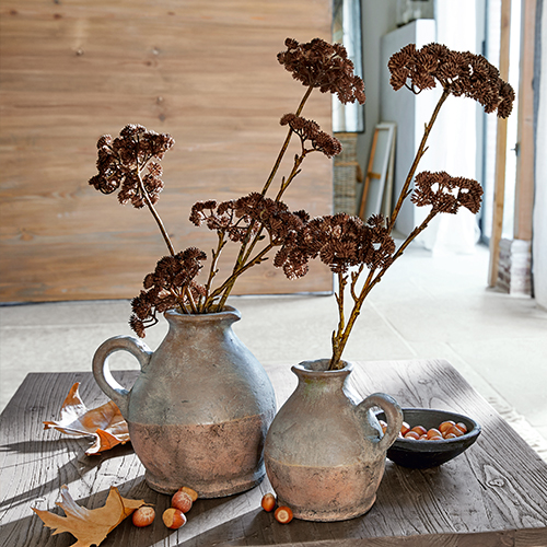 Deux pichets en céramique gris-brun avec fleurs séchées sur une table en bois avec des noisettes