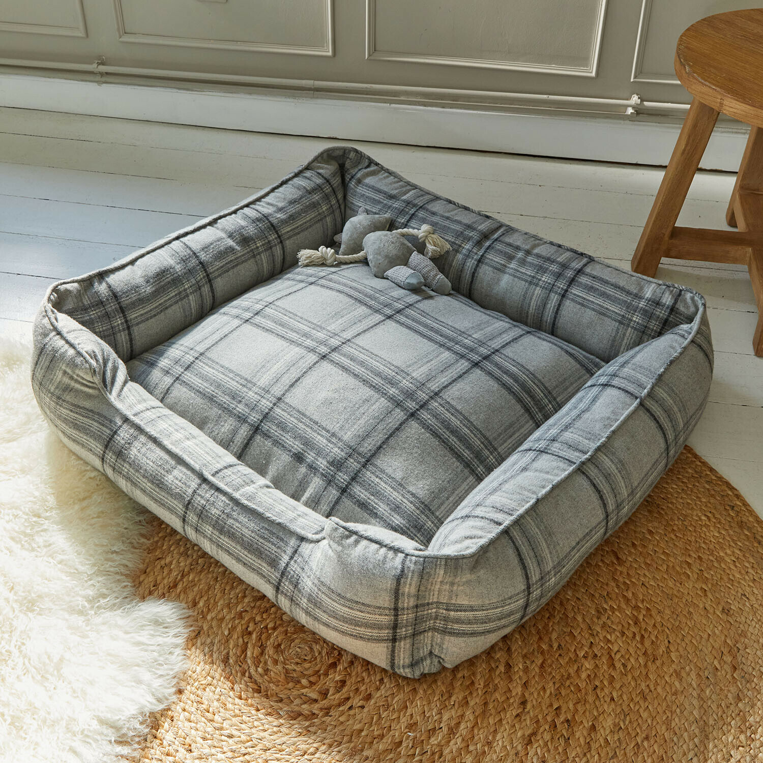Lit pour animaux Creswyn Panier pour chien gris à carreaux en tissu doux posé sur un tapis tressé dans une pièce lumineuse