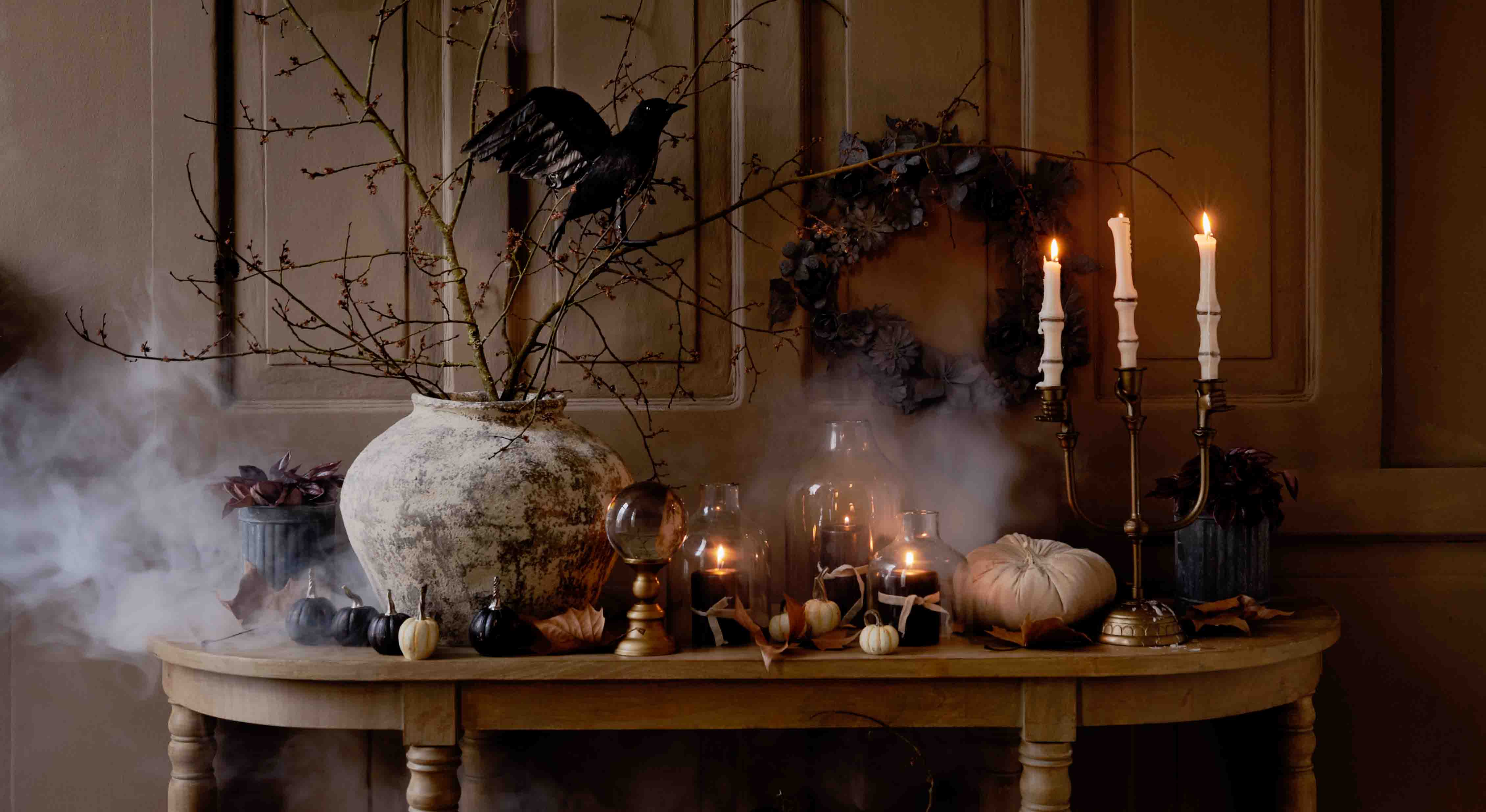 Table rustique décorée avec citrouilles, bougies et branches dans un vase en céramique, ambiance automnale