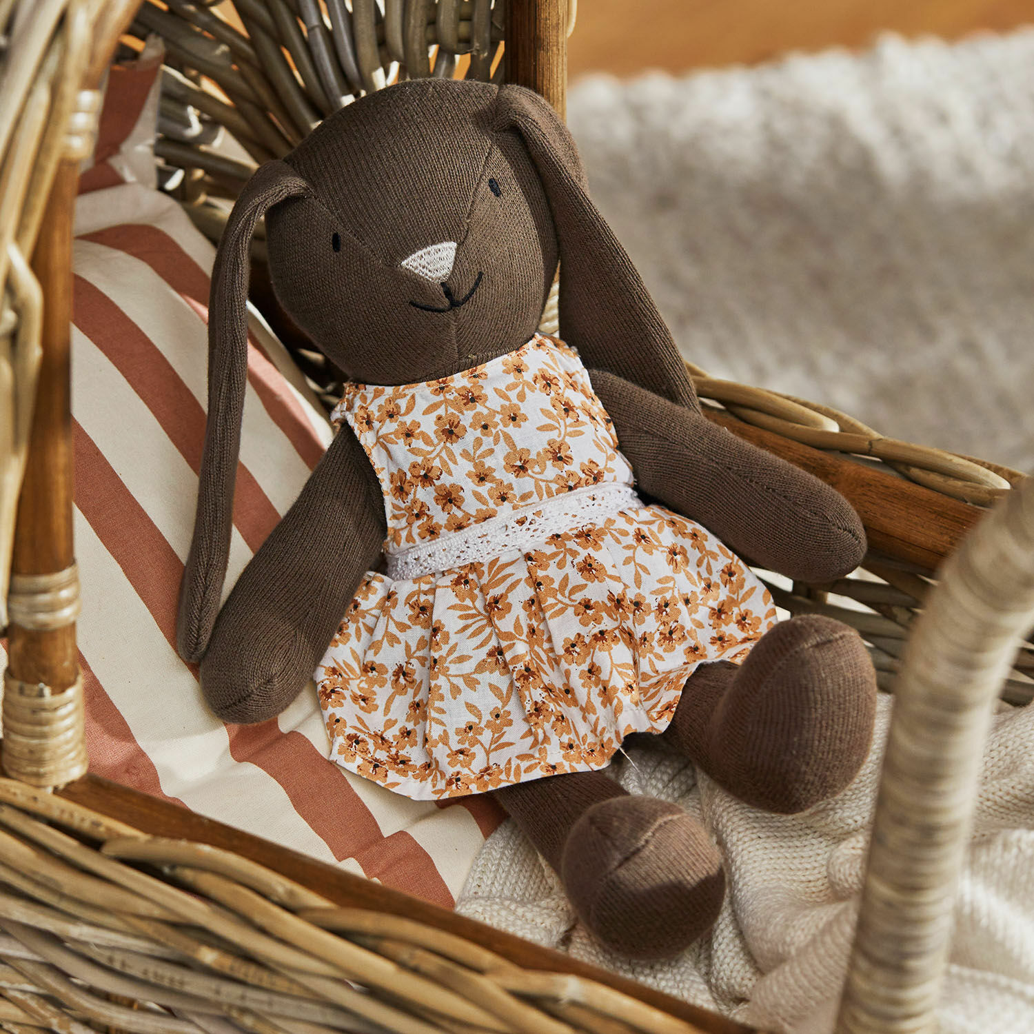 Peluche Pippaloo Lapin en peluche marron avec robe fleurie assis sur un fauteuil en osier avec coussin rayé