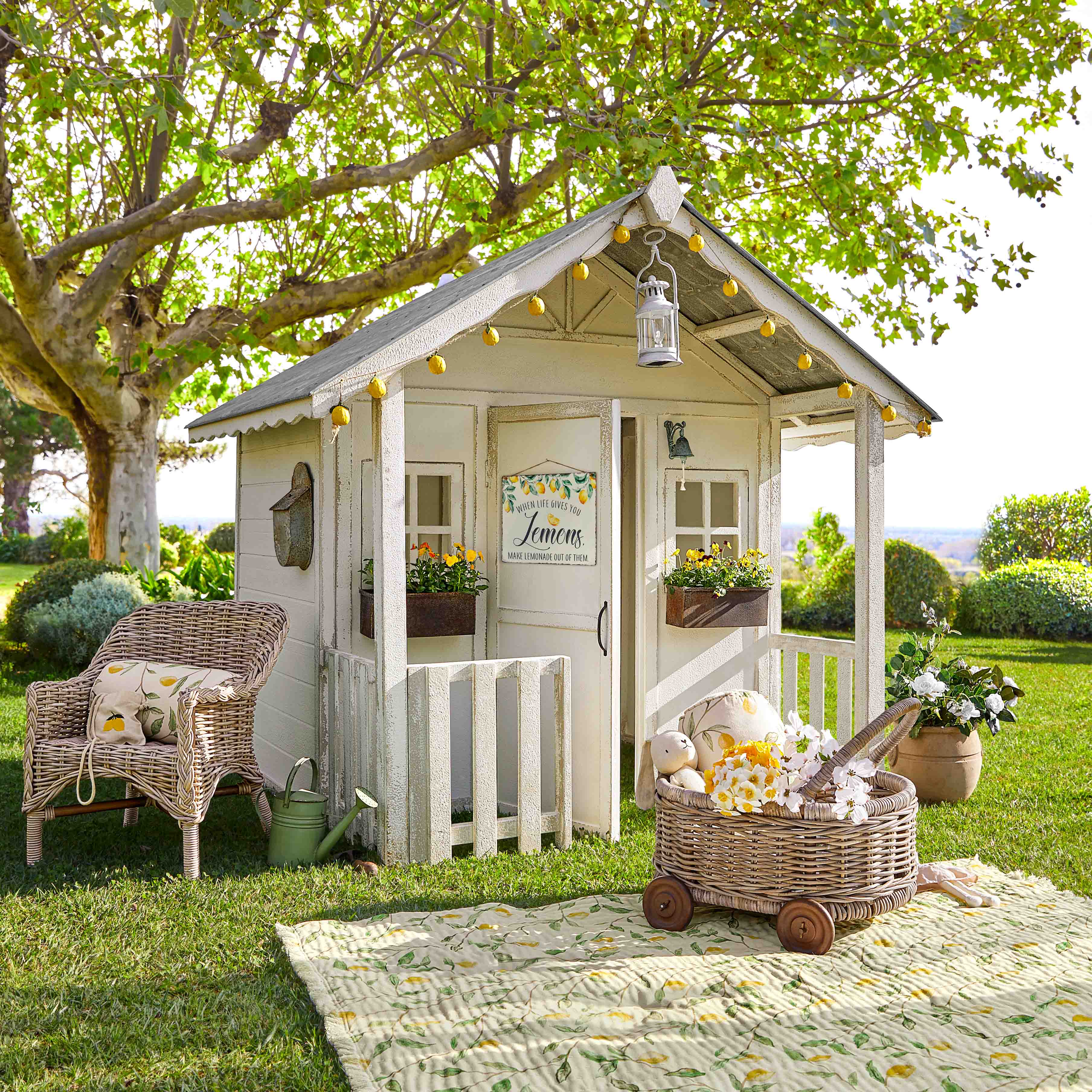 Maisonnette de jardin blanche en bois avec décorations citron et fauteuil en osier sur pelouse verte