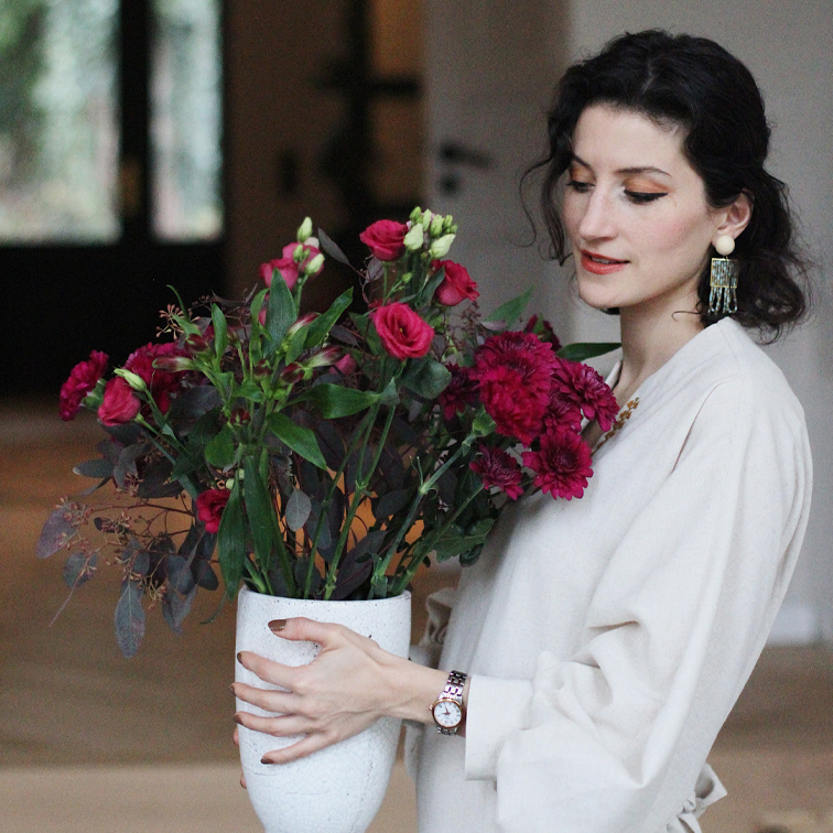 Femme en chemise claire tenant un vase en céramique blanche avec des fleurs rouges, décoration intérieure élégante